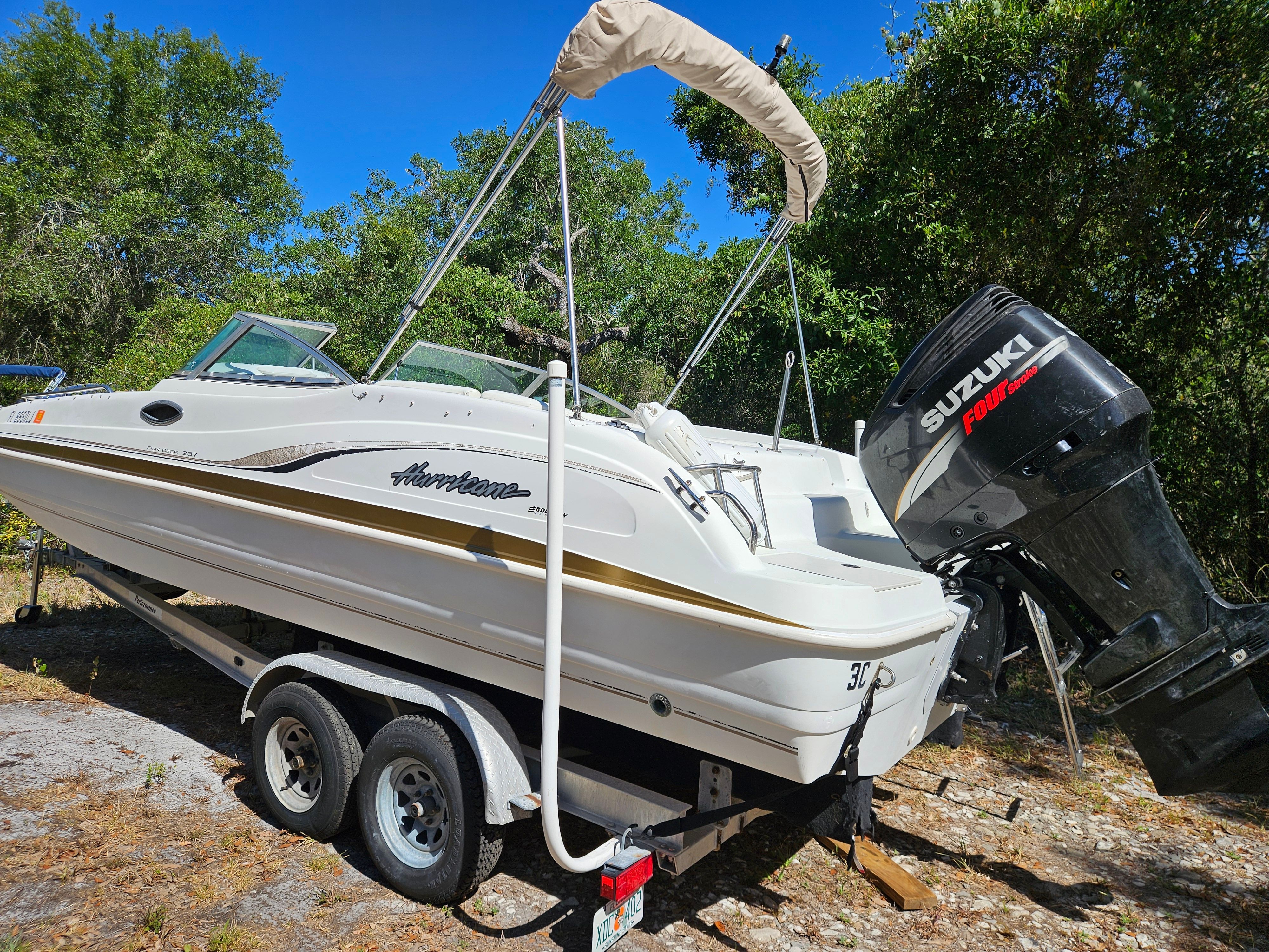 A 2001 Hurricane 237 boat on a trailer, surrounded by trees.