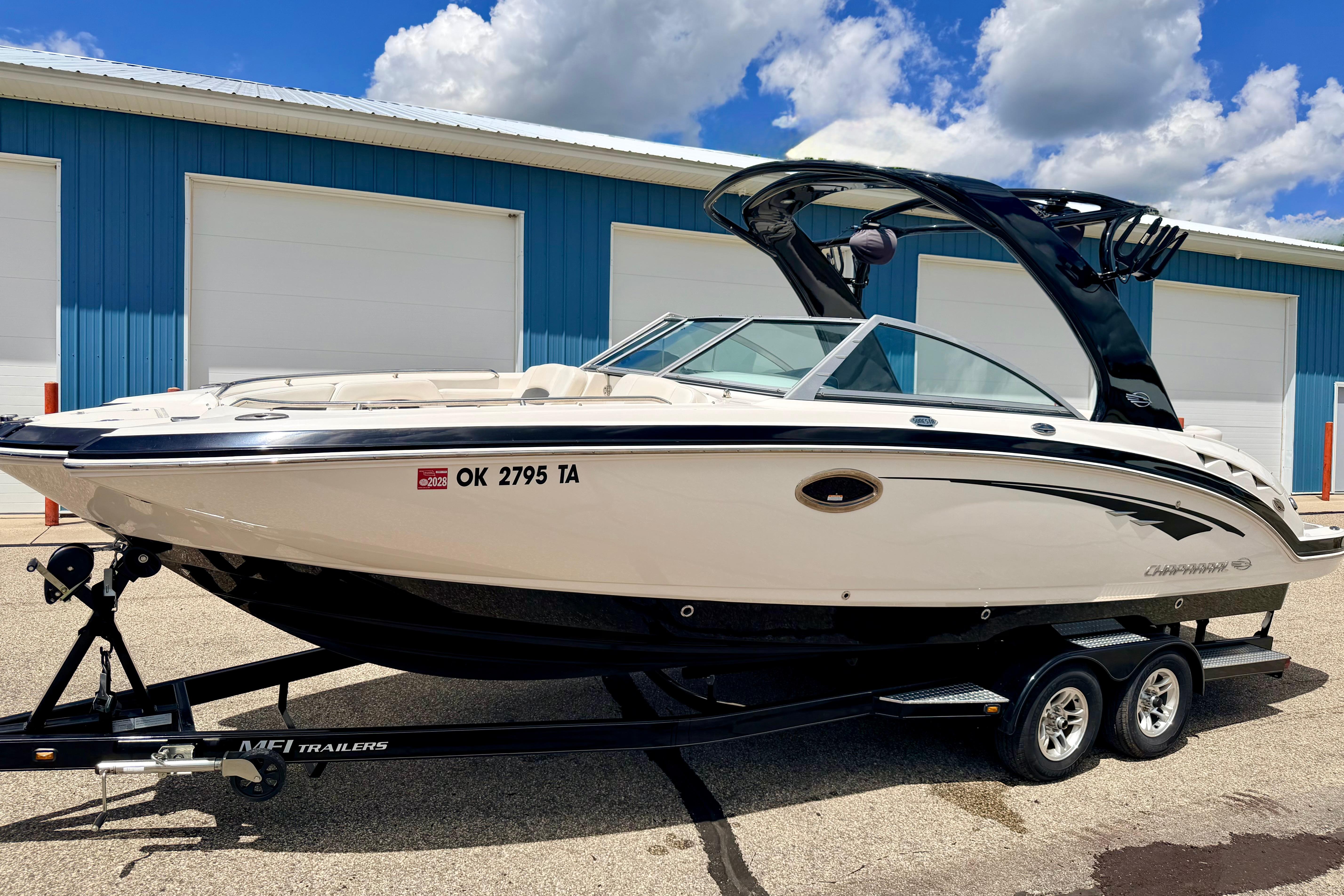 2015 Chaparral Sunesta 264 boat on trailer, parked near blue building under cloudy sky.