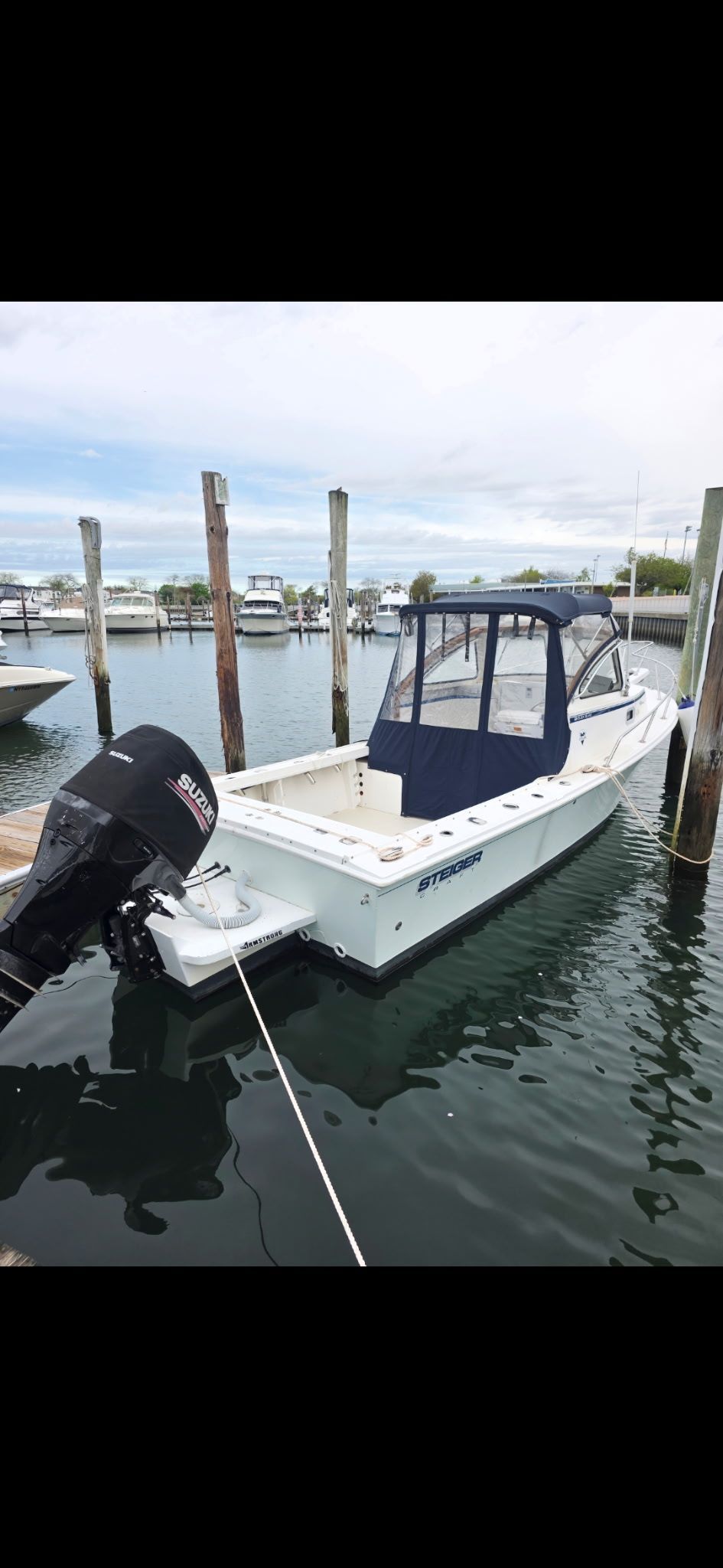 A white boat with a blue cover docked in a harbor, surrounded by pilings.