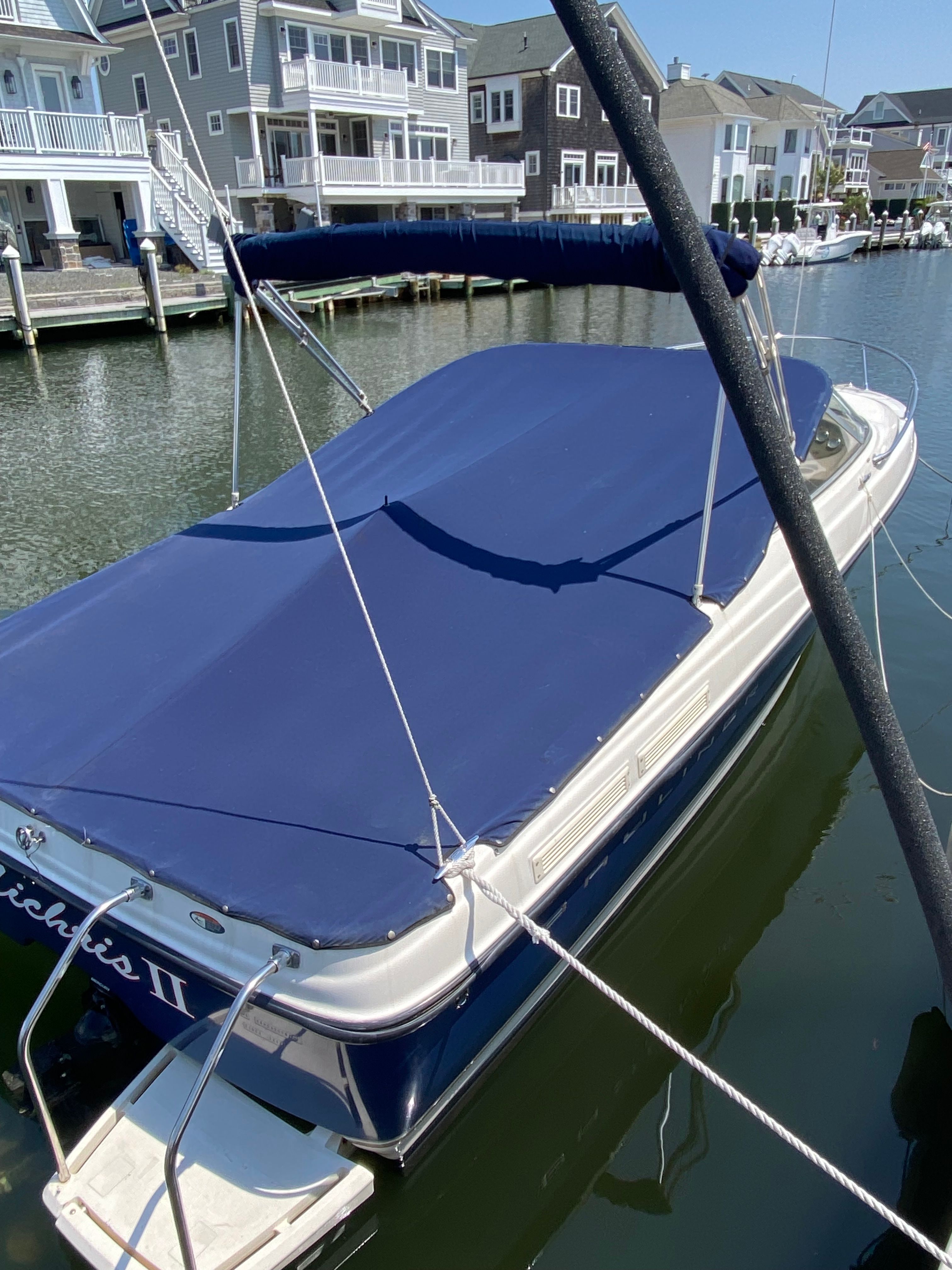 A 2003 Bayliner 2152 is docked, covered in blue, surrounded by waterfront homes.