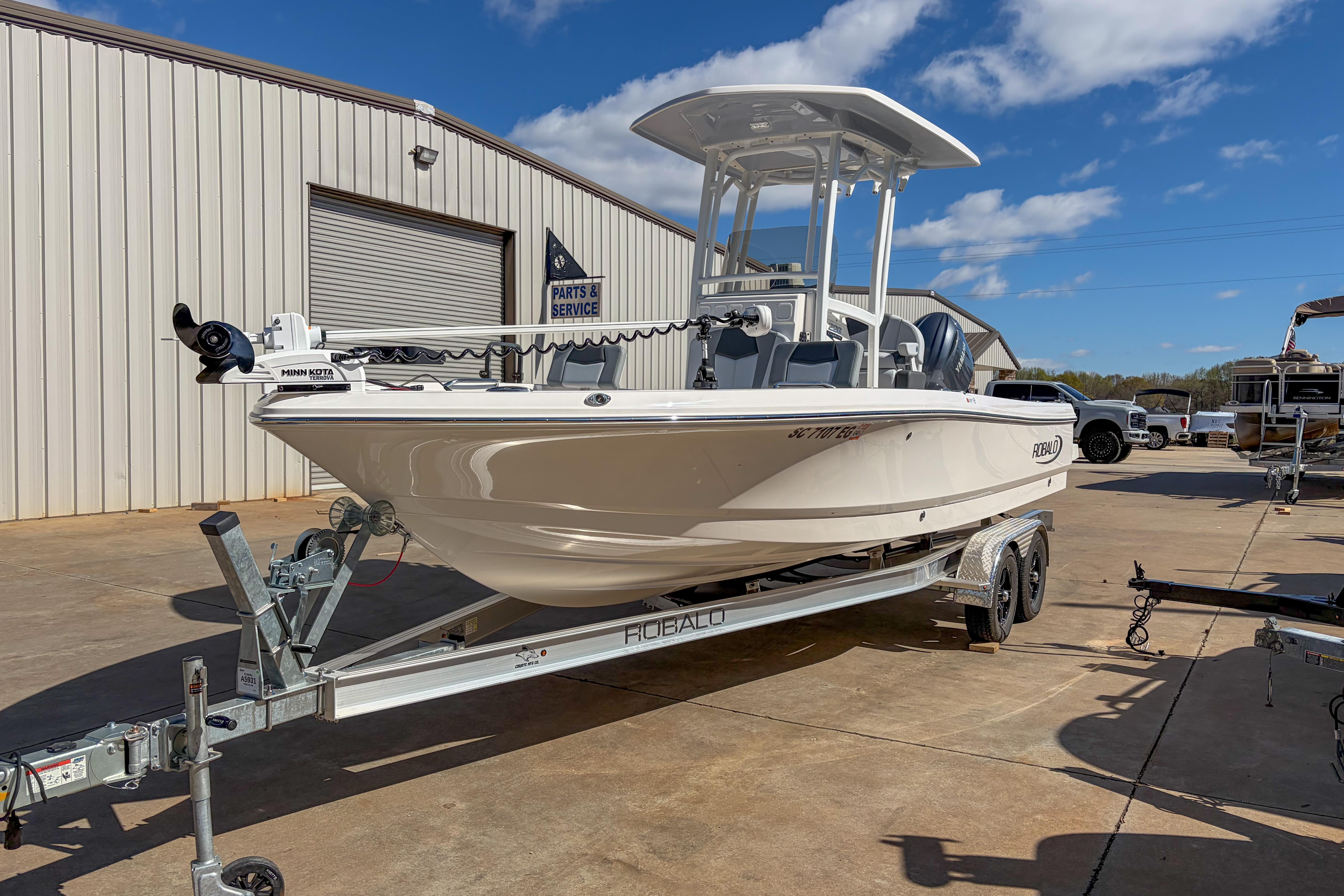 2025 Robalo 226 Cayman boat on trailer, parked outside service building under blue sky.