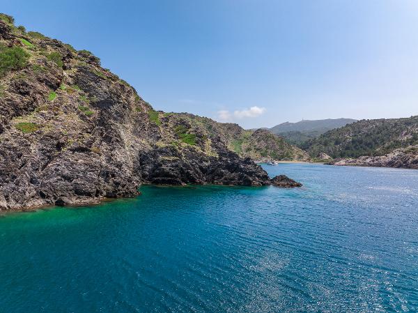 Coastal landscape with clear blue water and rocky cliffs under a bright sky.