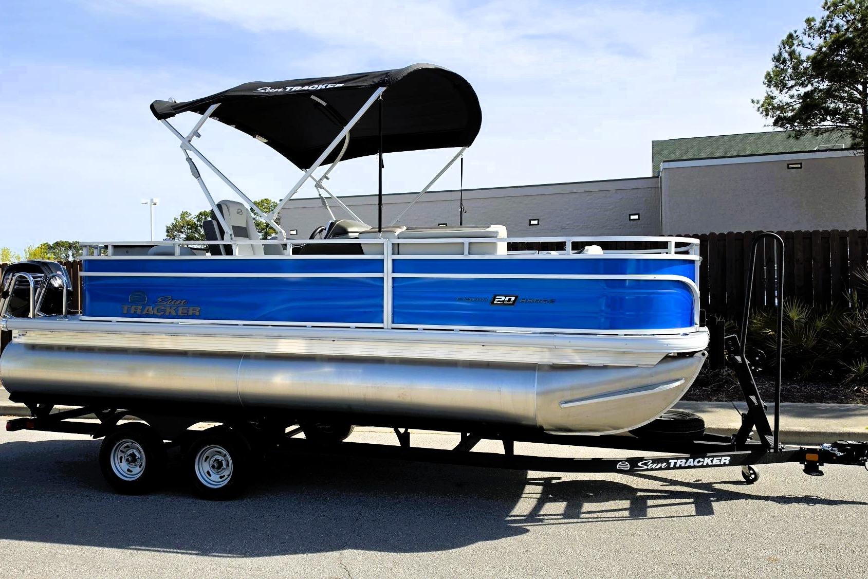 2026 Sun Tracker Fishin' Barge 20 DLX pontoon boat on trailer, blue and silver design.