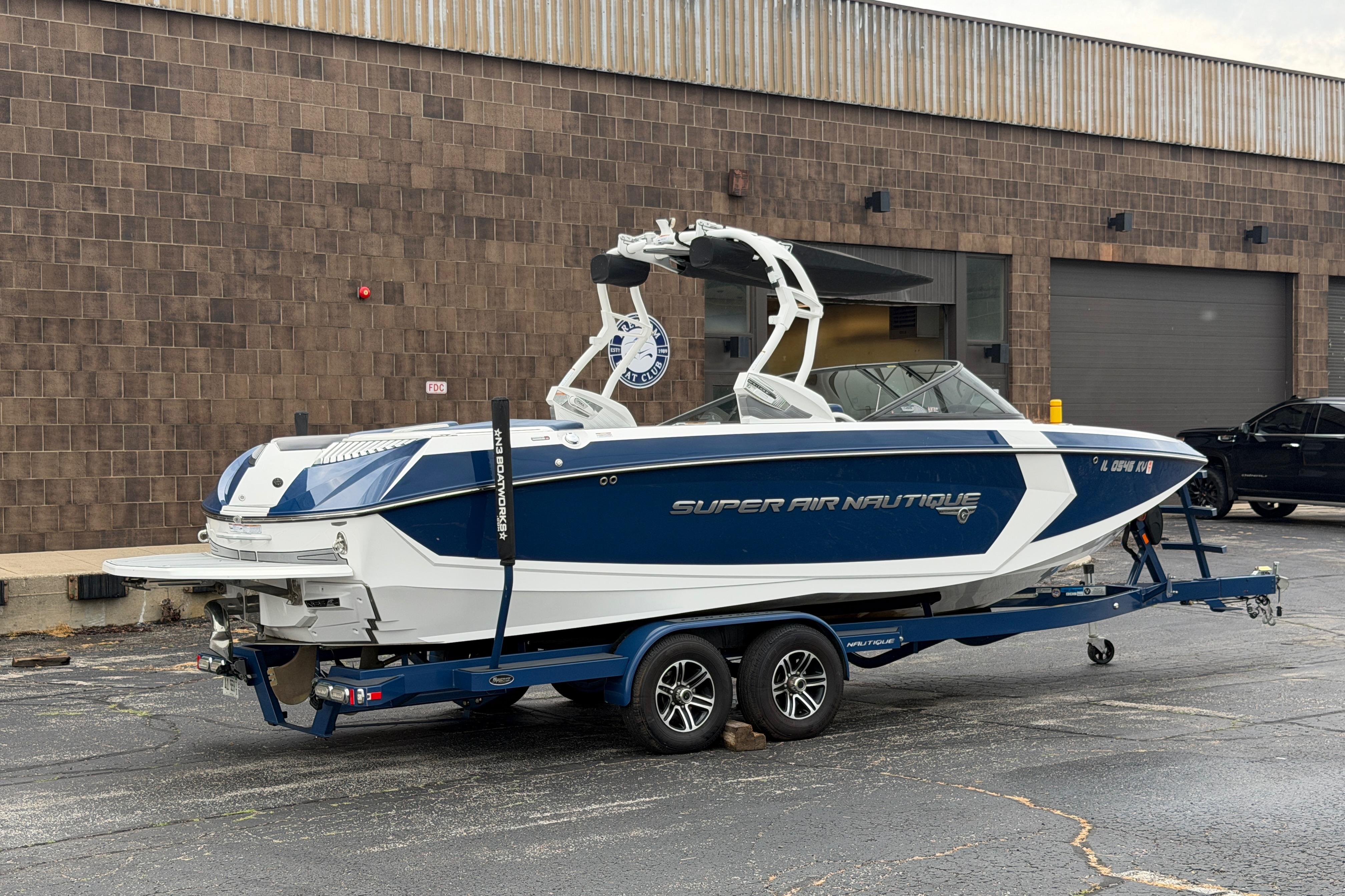 2016 Naitique G25 boat on trailer, parked outside industrial building.