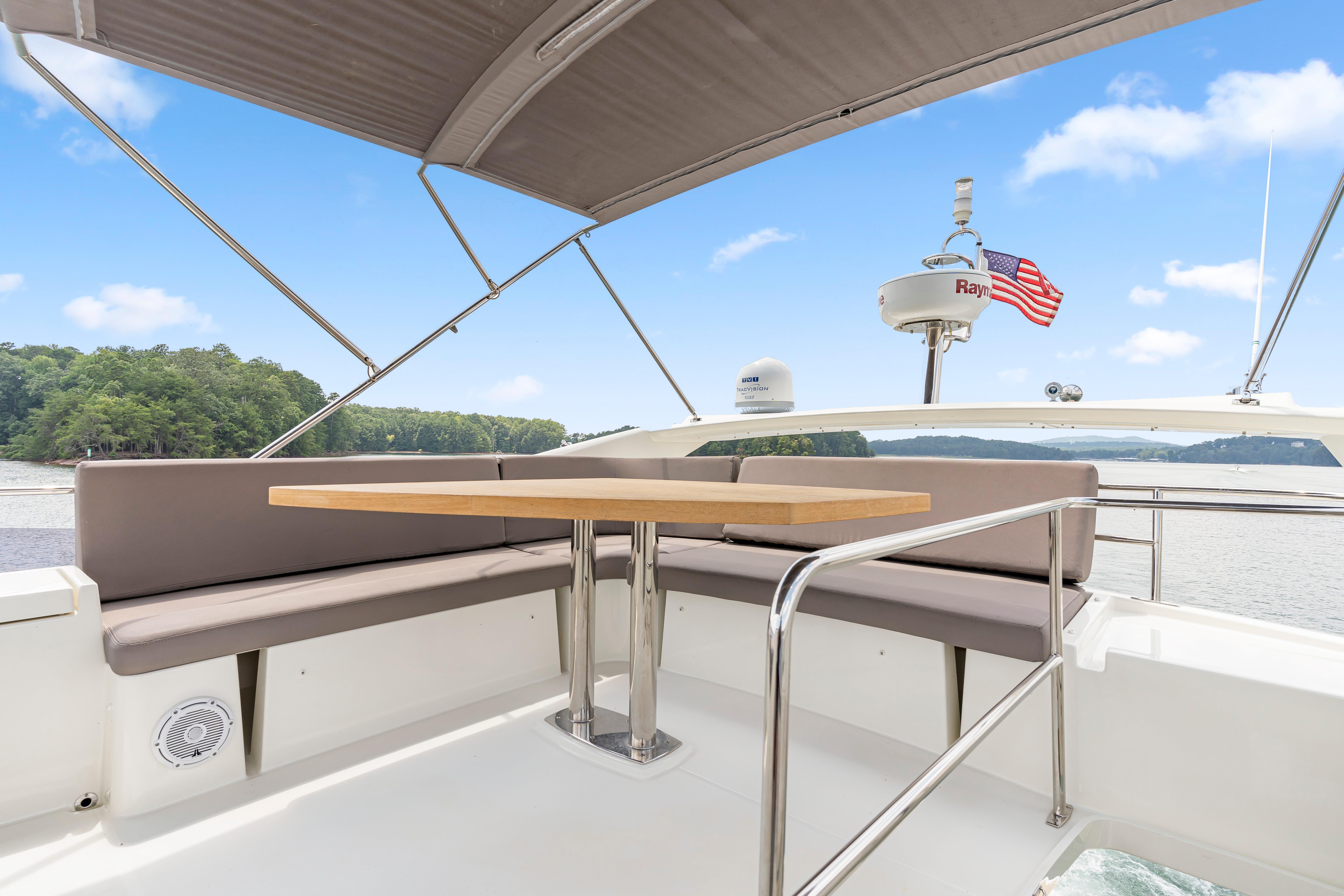 Flybridge seating area on 2017 Prestige 500 yacht with table, under a canopy, near scenic waterway.