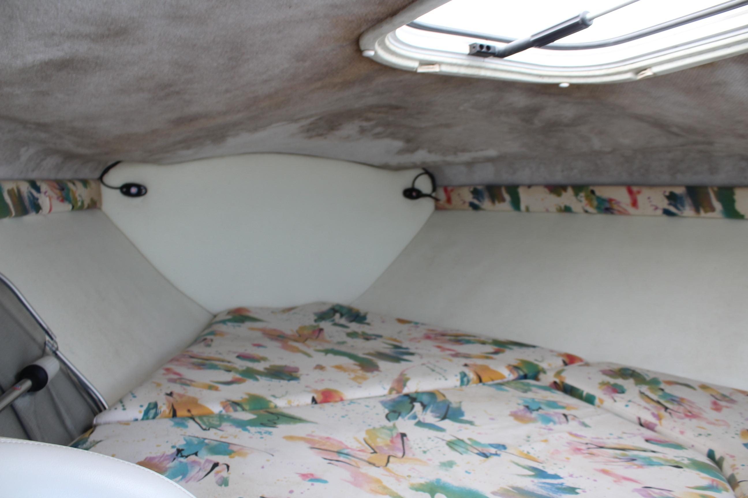 Interior cabin of a 1996 Baja 232 boat with colorful bedding and overhead hatch.
