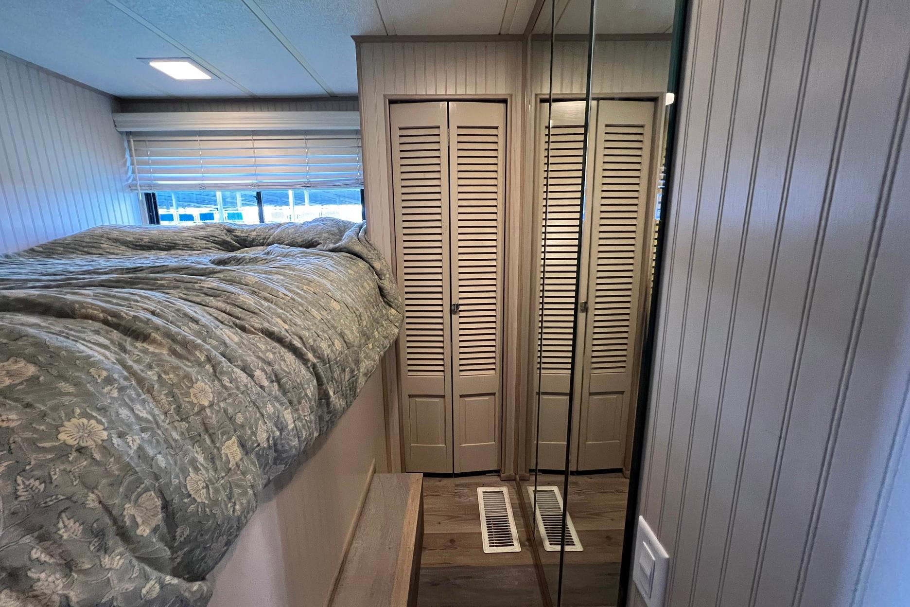 Cozy 1993 Sumerset houseboat interior with bed, mirrored closet, and wooden paneling.