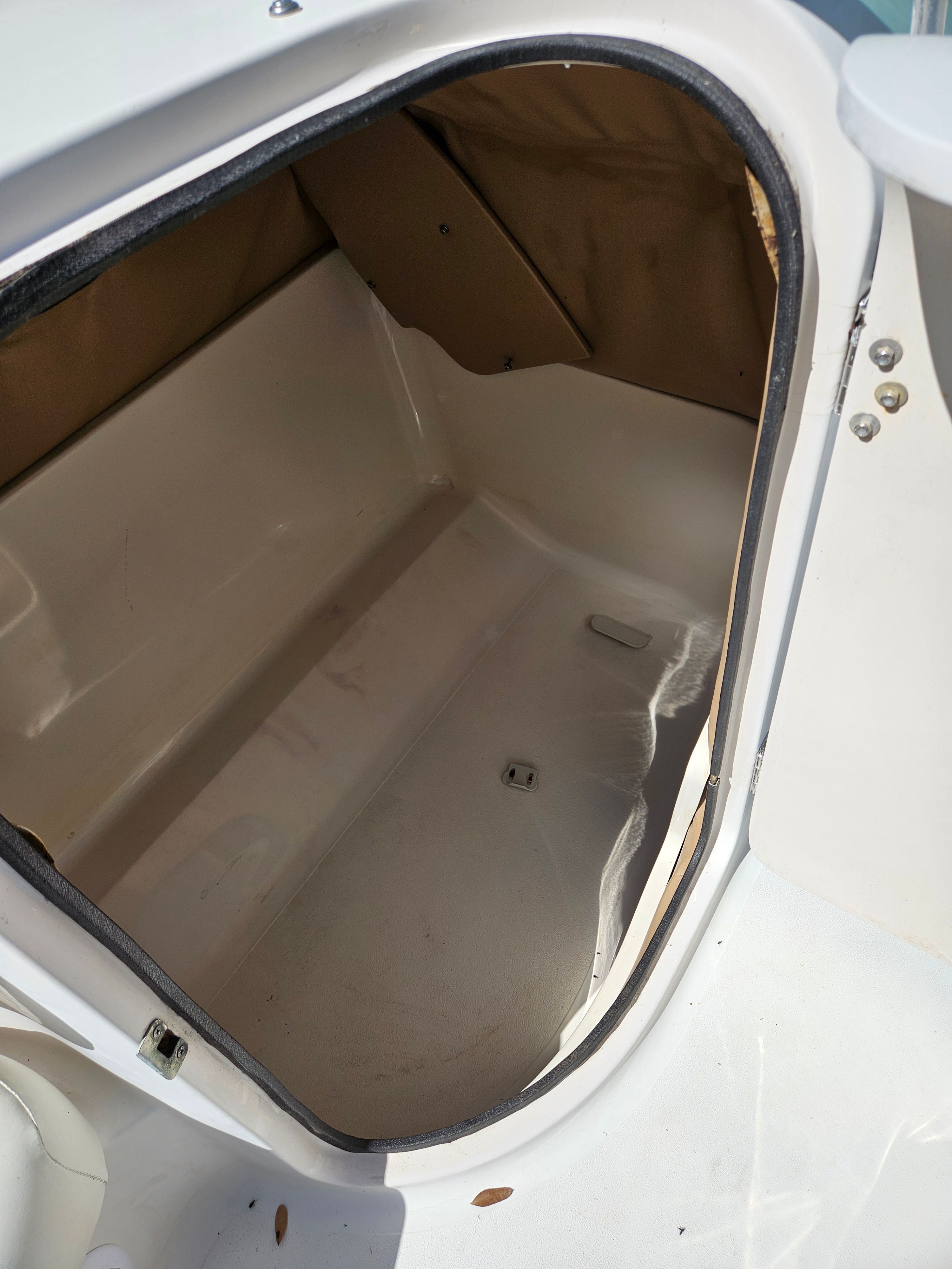 An open storage compartment on a boat with a white interior and brown cover.