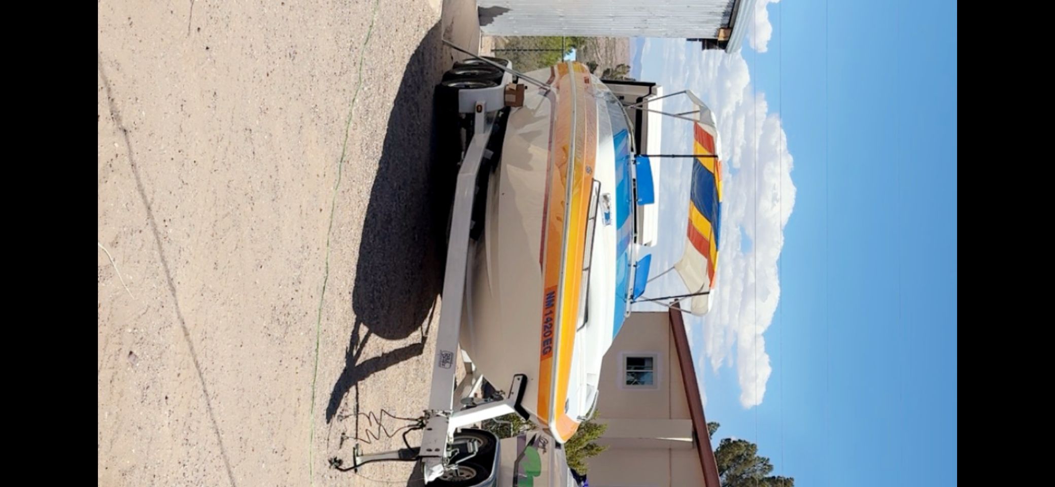 A 2001 Advantage 27 Victory boat on a trailer, with colorful sunshade, sits on a gravel path.