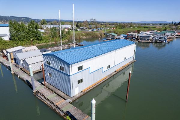 Aerial view of 1985 Custom Larson Boathouse on calm water, blue roof, surrounded by docks.