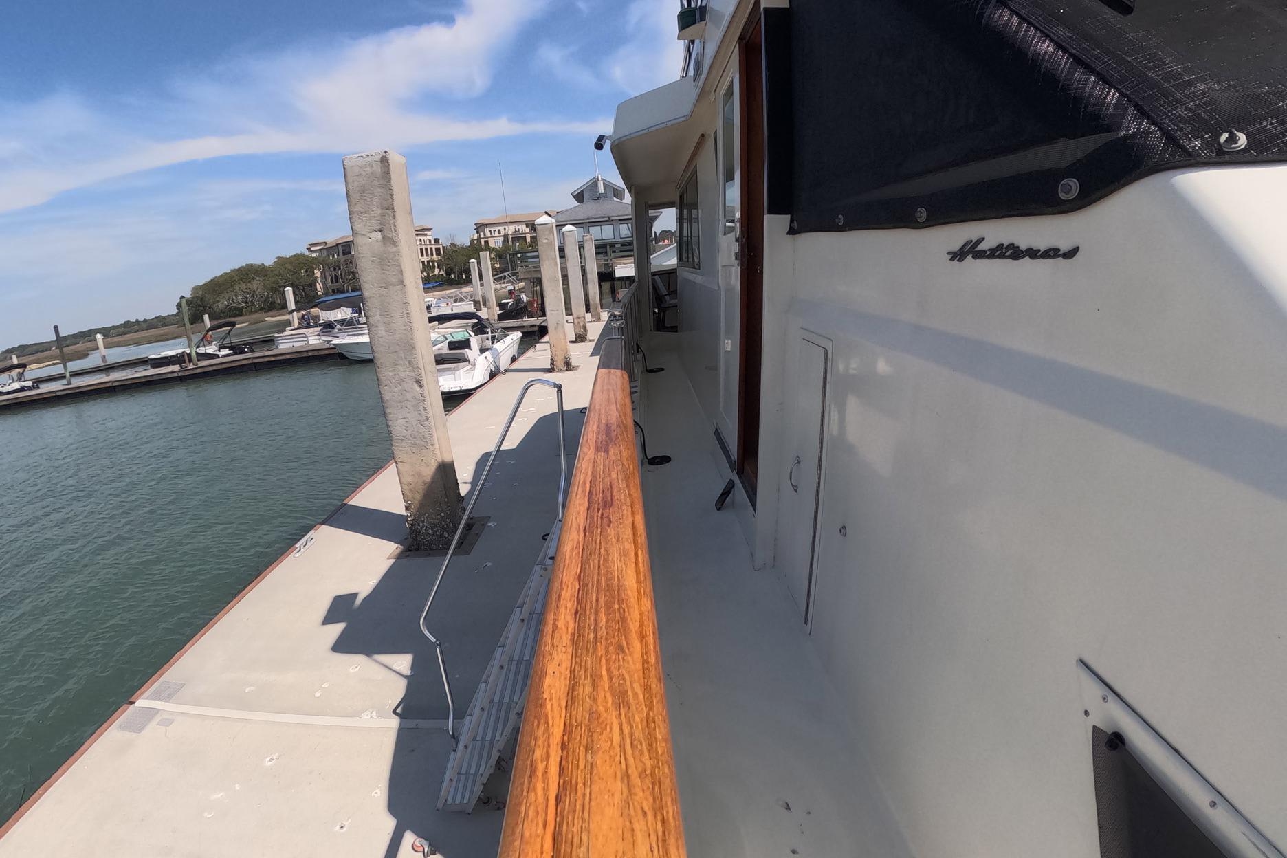 1987 Hatteras 54 Motor Yacht docked at marina, showcasing sleek design and wooden railings.