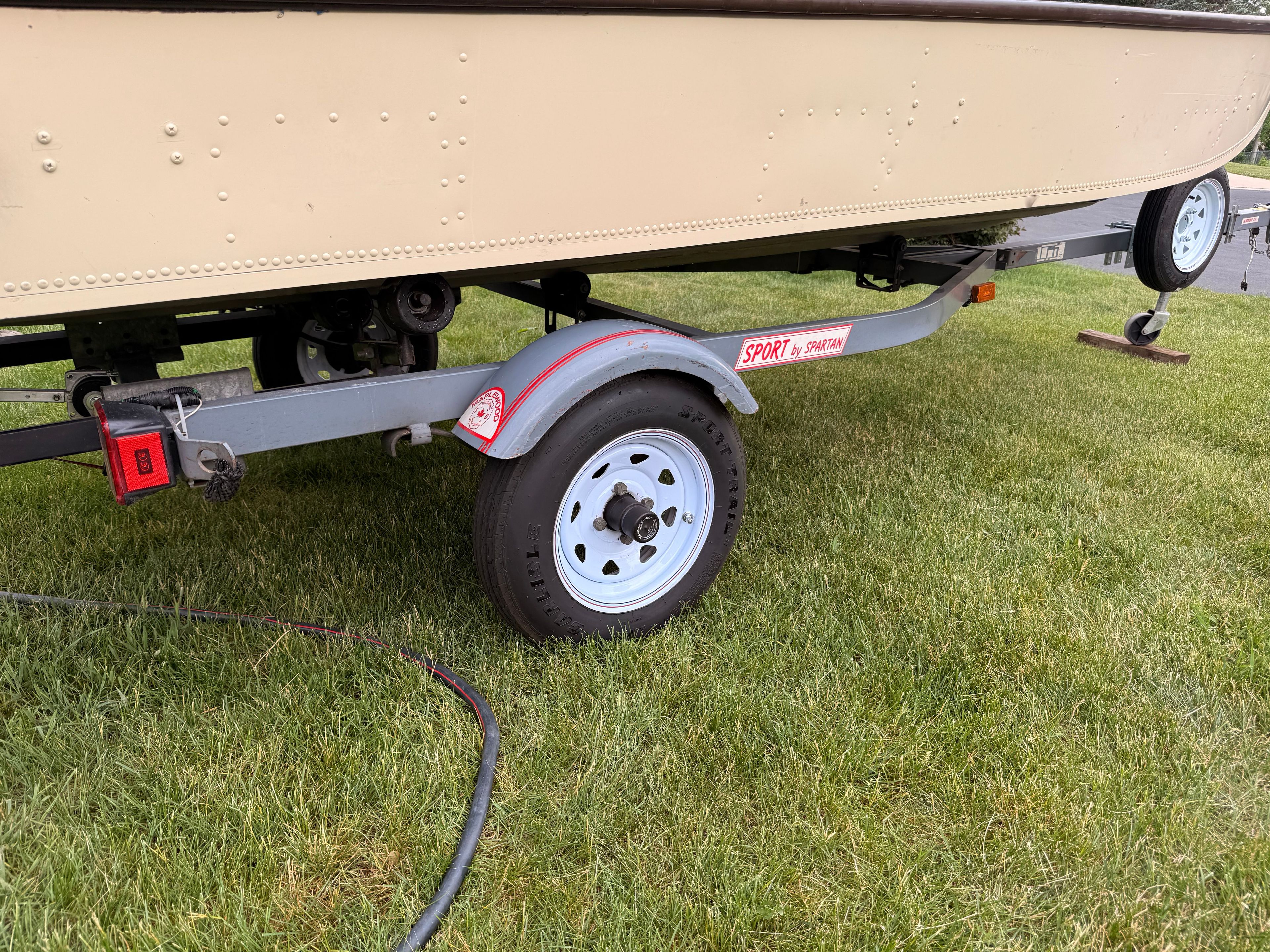 A 1985 Grumman boat on a trailer on grass.