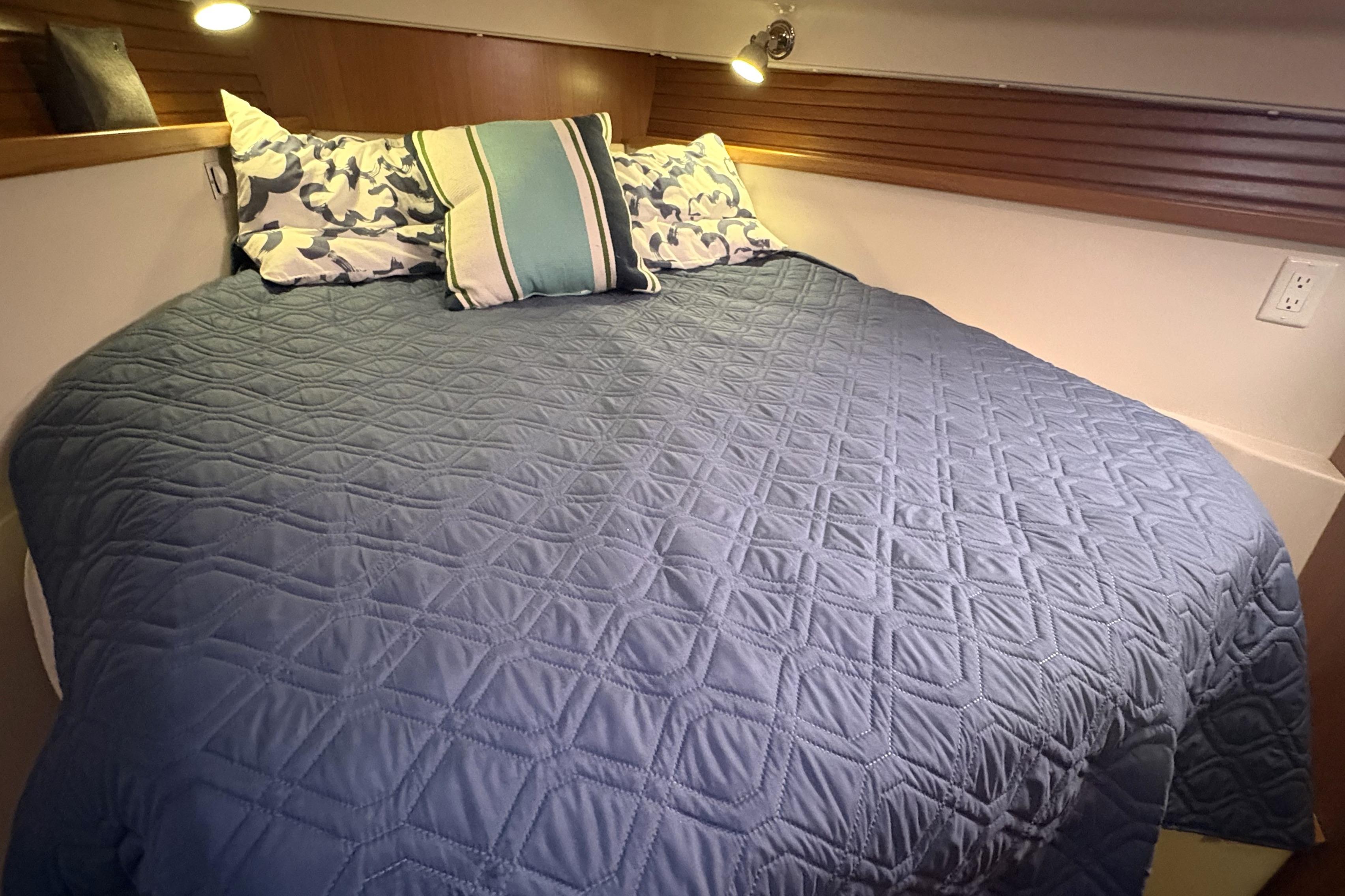 Cozy cabin bed in 2011 Catalina 355 yacht with blue quilt and decorative pillows.