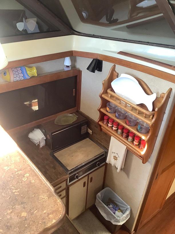 Compact kitchen area in a 1982 Trojan F32 boat with wooden shelves and spice rack.
