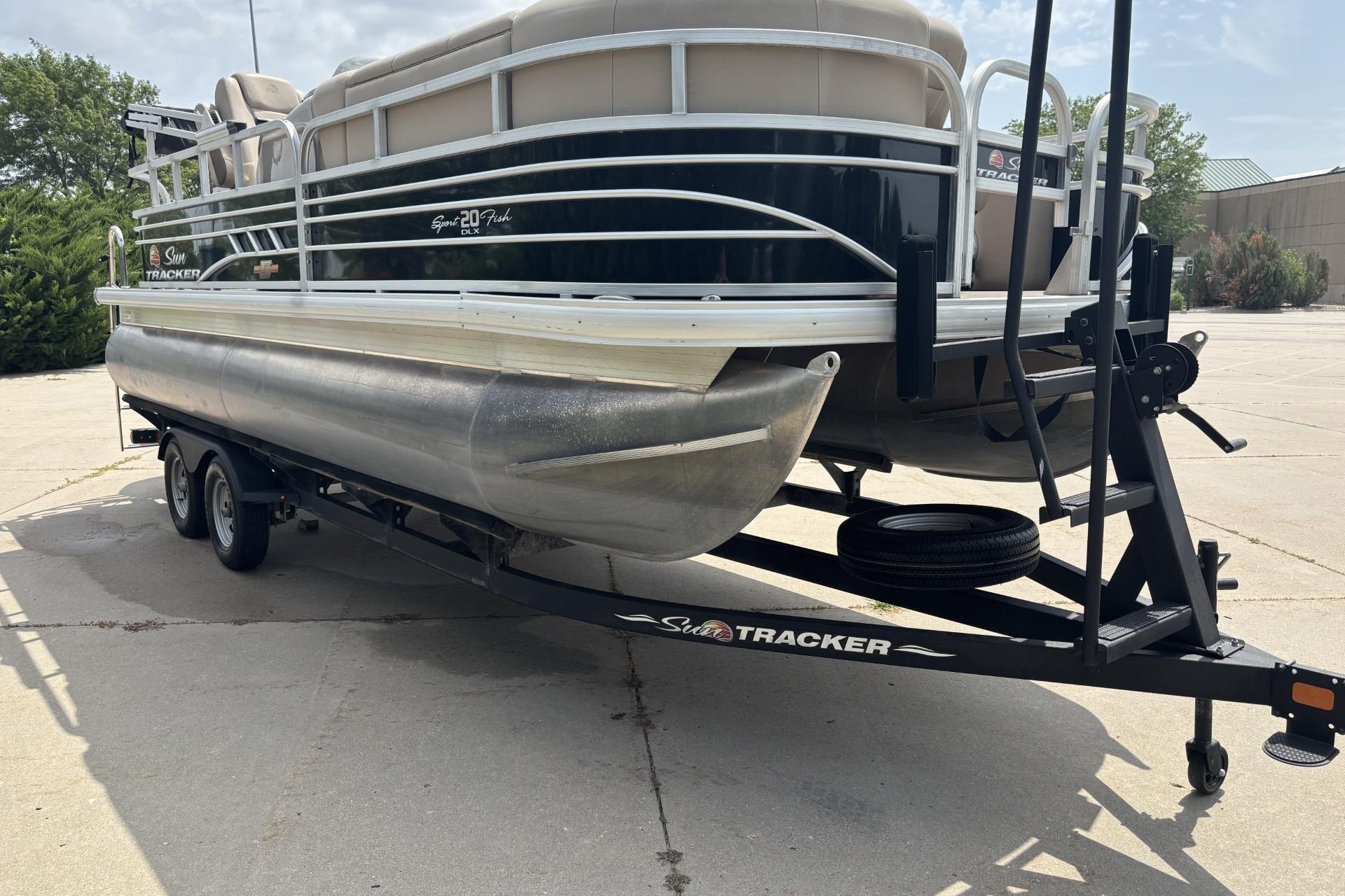 2023 Sun Tracker SportFish 20 DLX pontoon boat on trailer, parked outdoors.