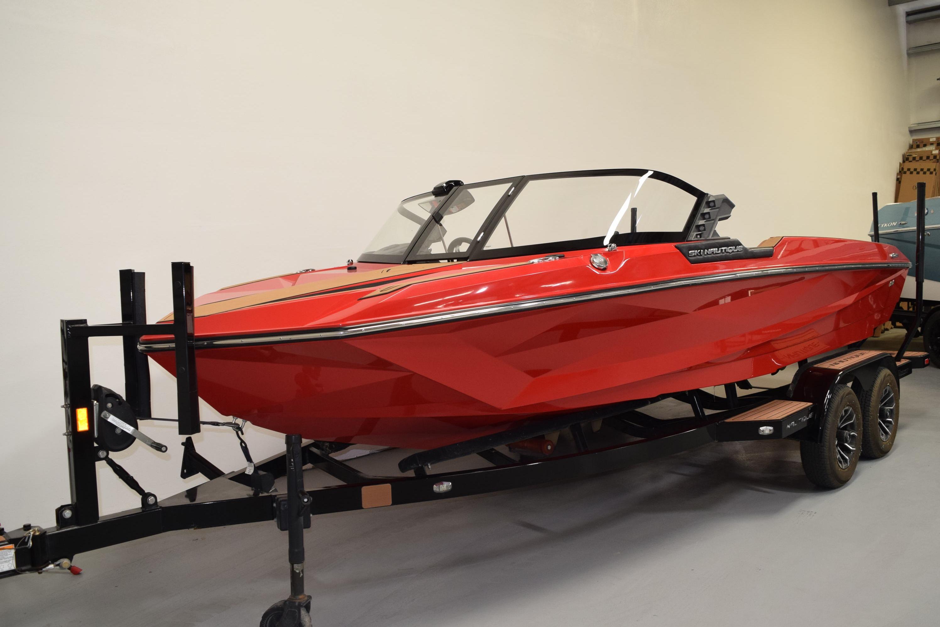 2024 Nautique Ski Nautique boat in vibrant red on a trailer, side view.