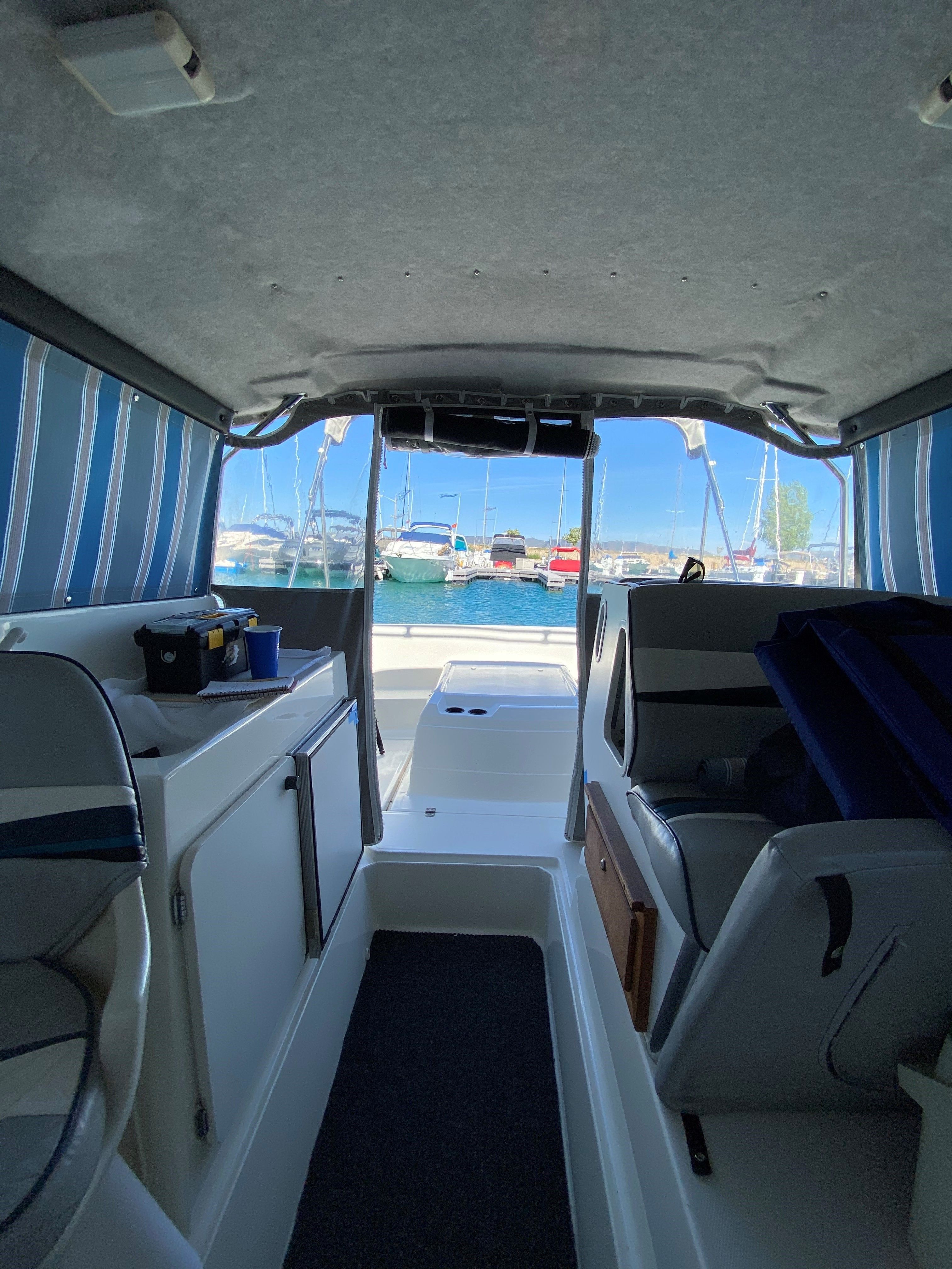 Interior of a 1991 Bayliner 2159 with blue and white striped curtains, overlooking a marina.