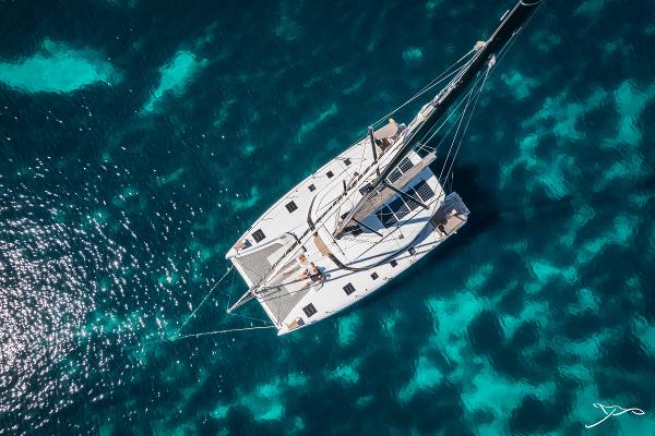 Aerial view of 2025 Nautitech 44 Open catamaran sailing on clear blue water.