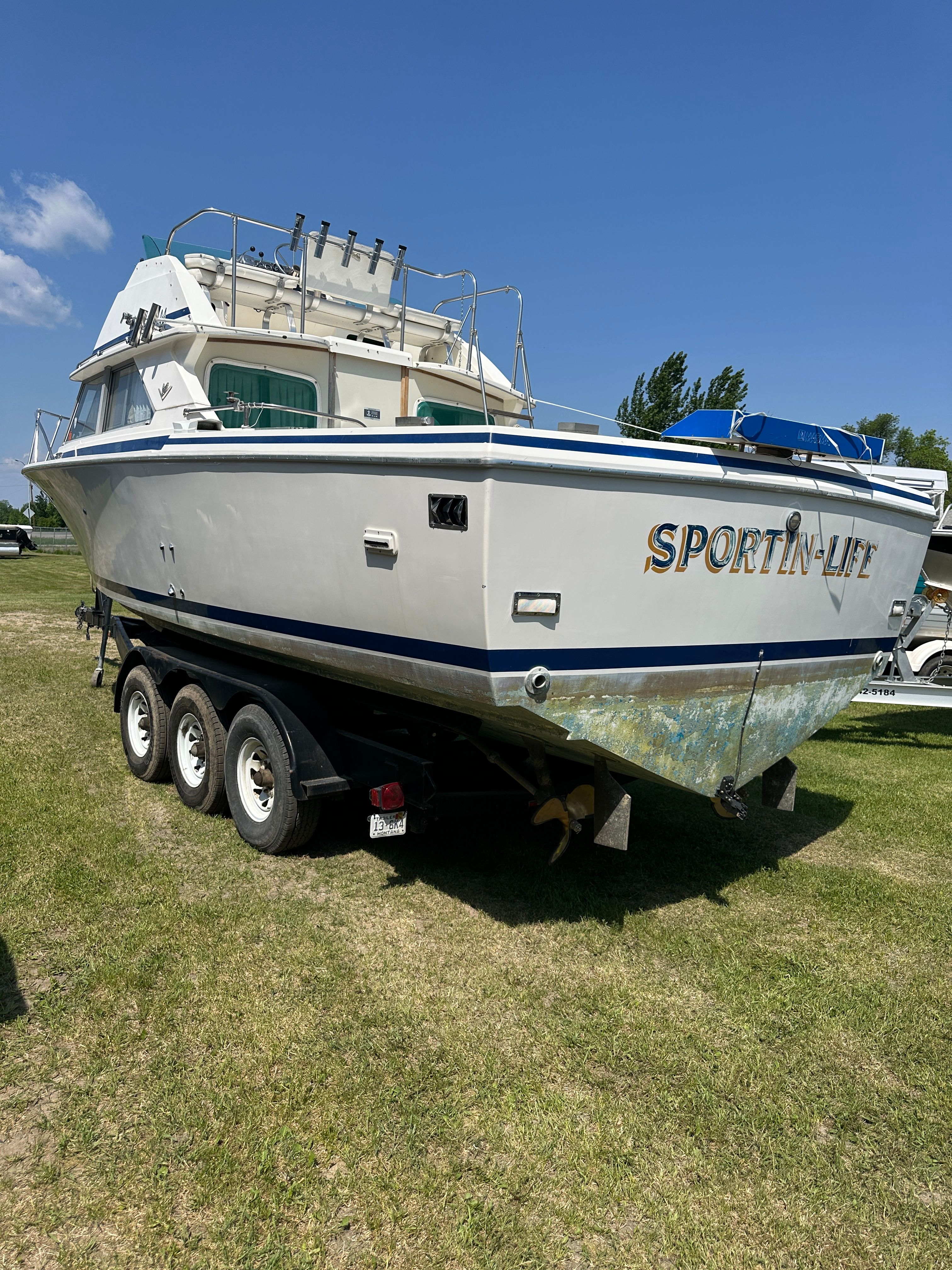 A 1983 Bertram Flybridge Cruiser on a trailer, parked on grass.