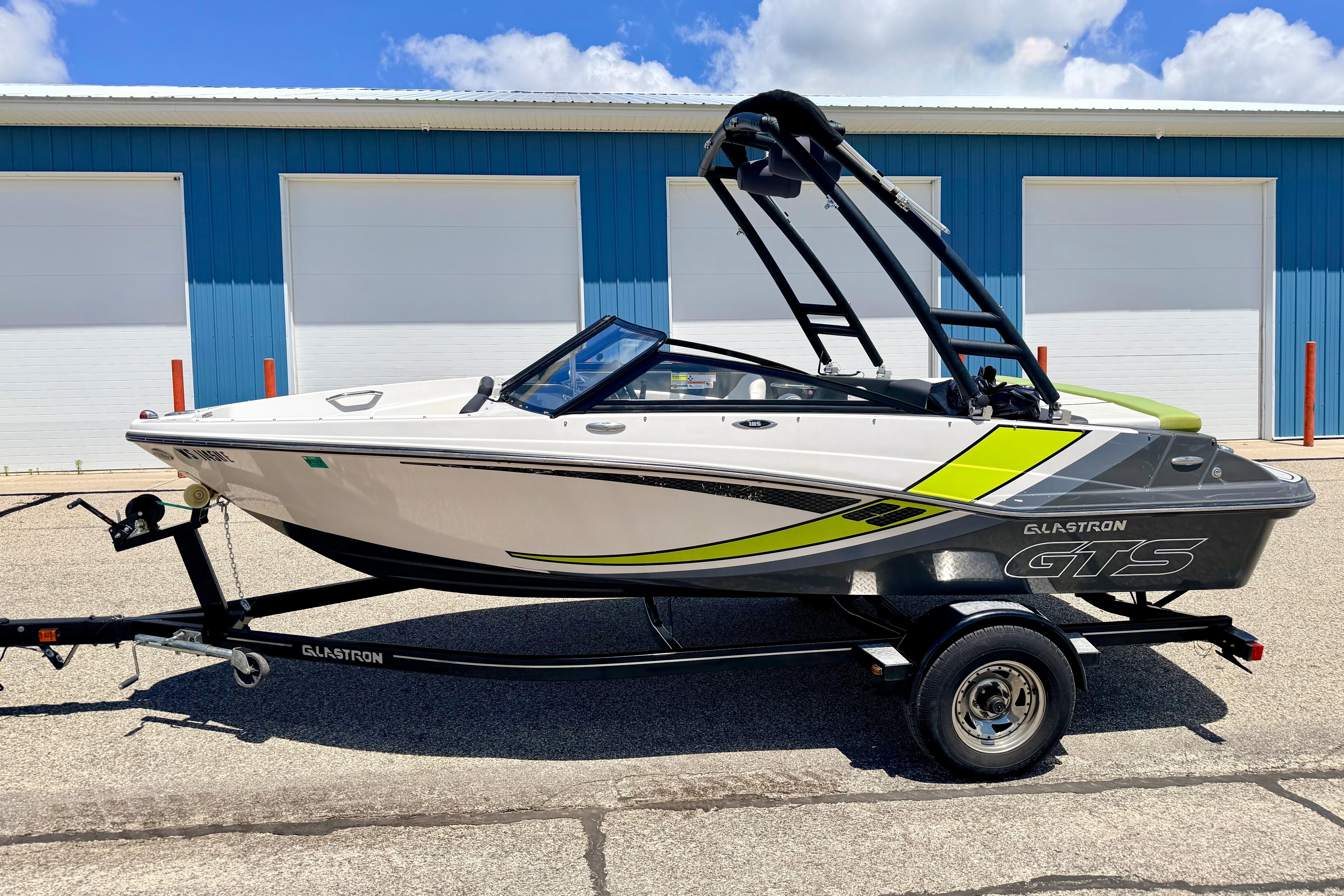 2018 Glastron GT 185 boat on trailer, parked outside blue building under clear sky.