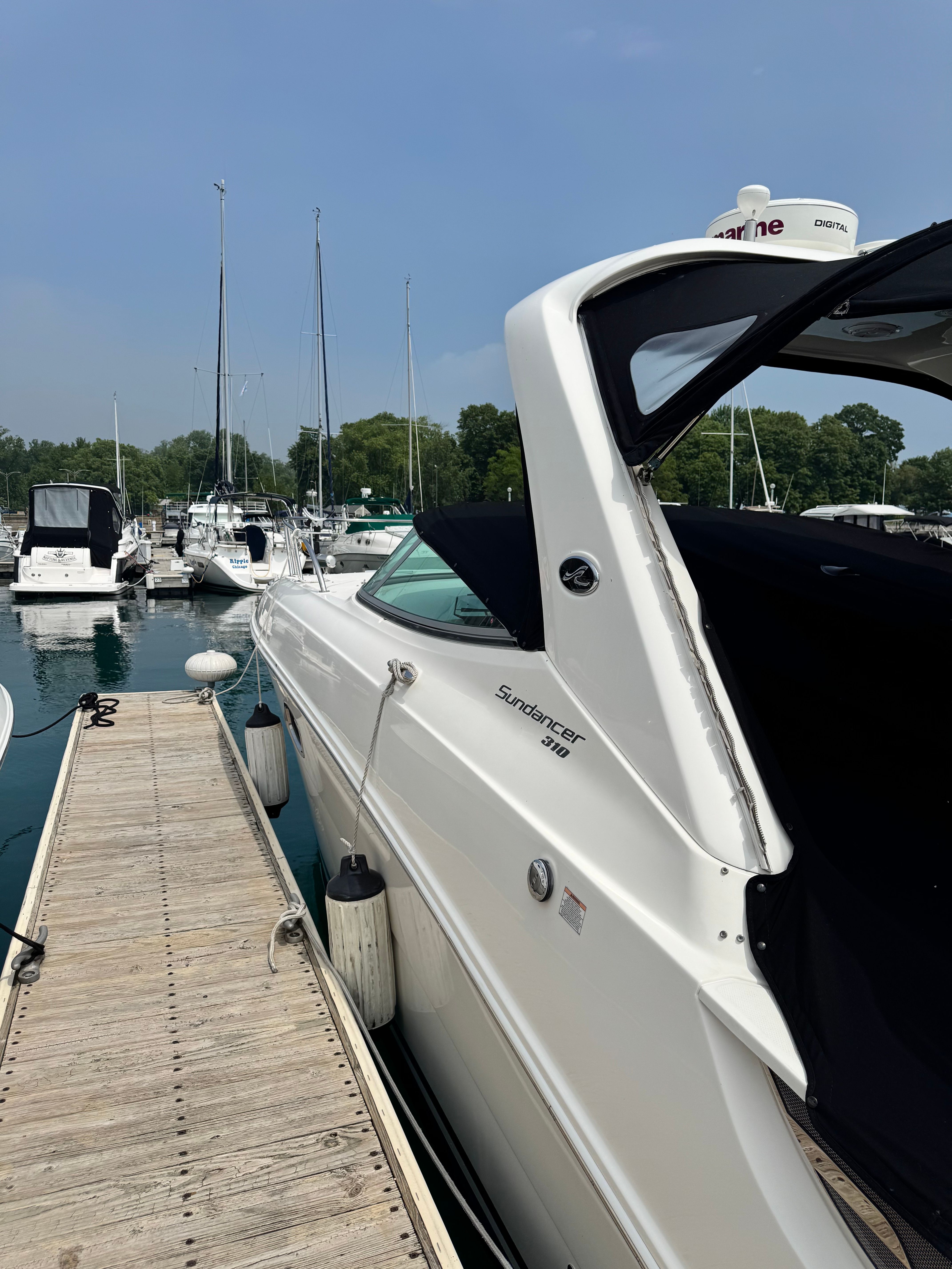 A white 2010 Sea Ray Sundancer 310 boat docked at a wooden pier in a marina.