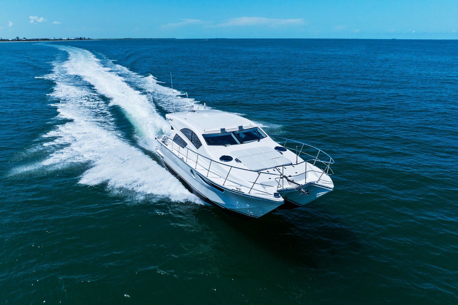 A white catamaran speeds across the blue sea, leaving a white wake behind.