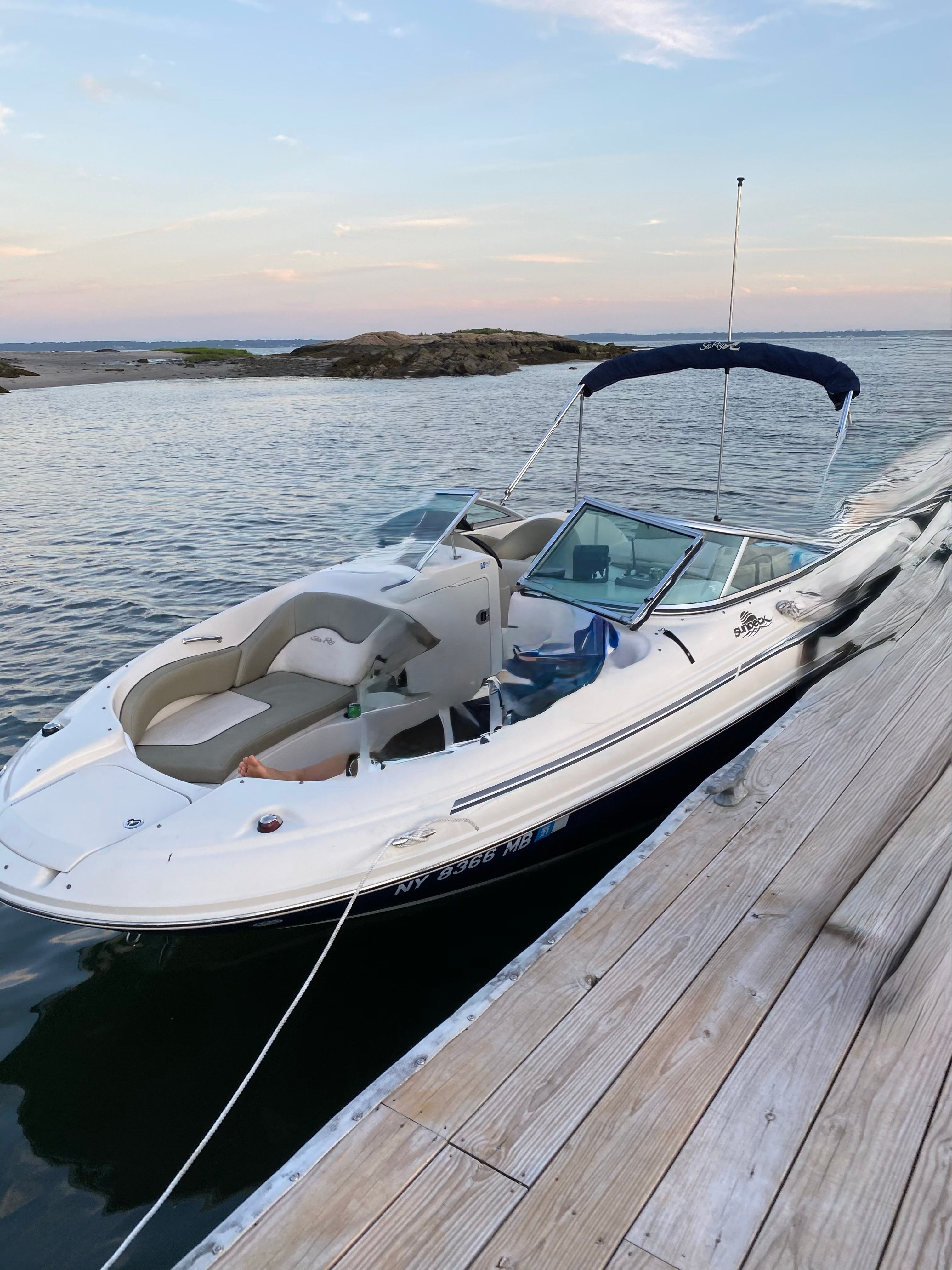 A 2005 Sea Ray Sun Deck 200 docked at a wooden pier. It features an open deck and blue canopy.