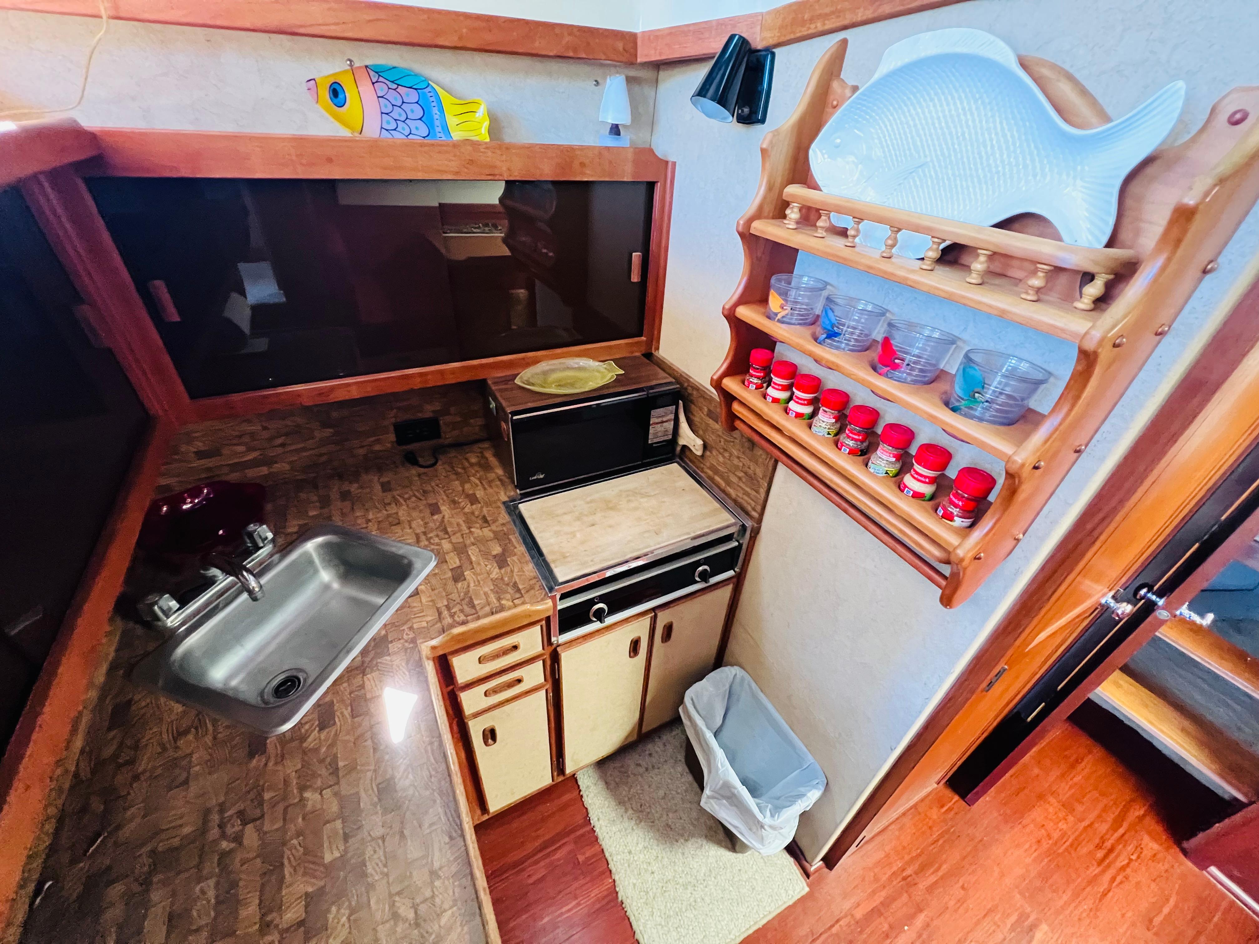 Compact kitchen in a 1982 Trojan F32 boat with sink, stove, and spice rack.