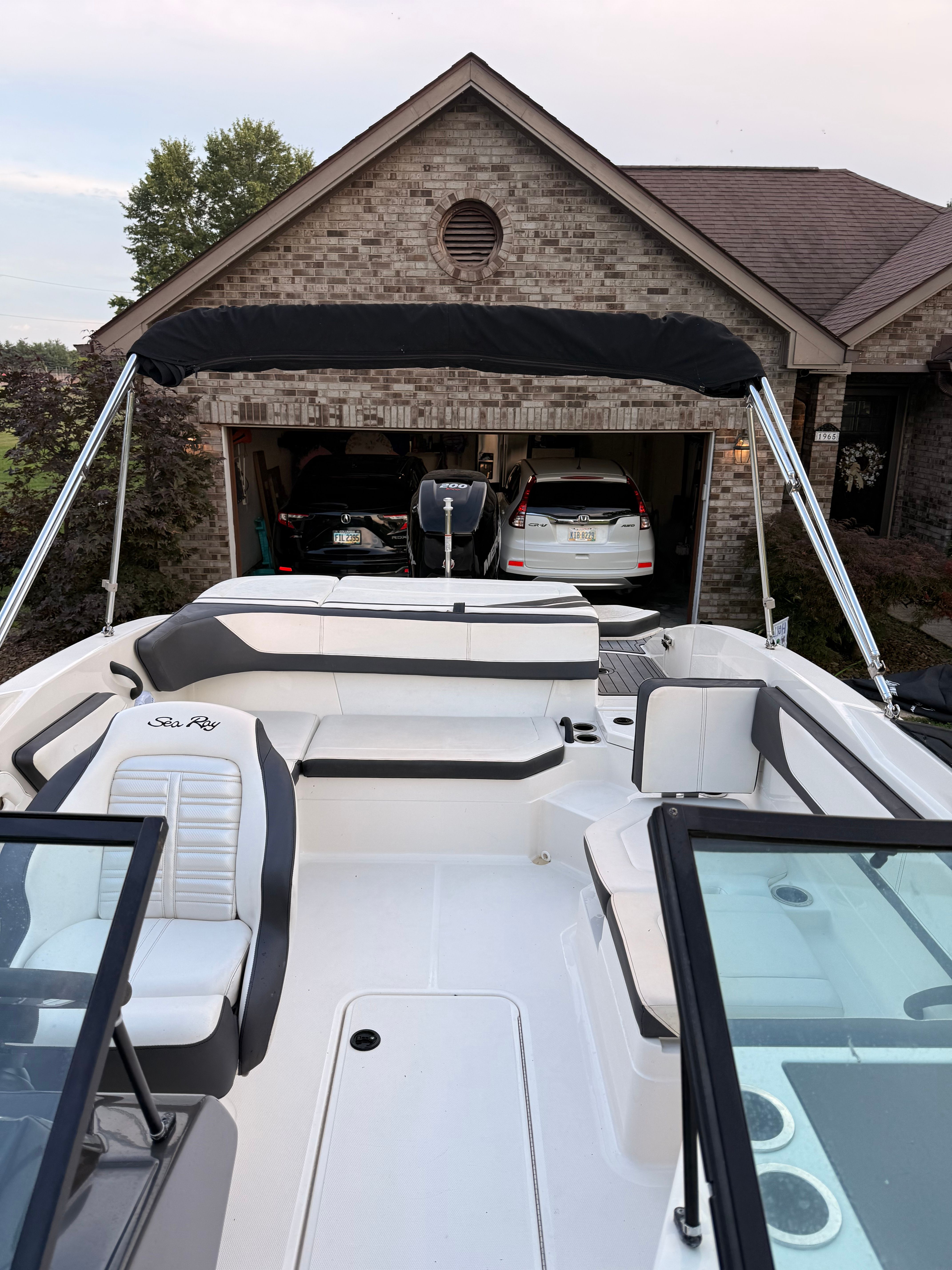 A 2016 Sea Ray SPX 210 Outboard is parked in front of a garage. It features white and gray upholstery.