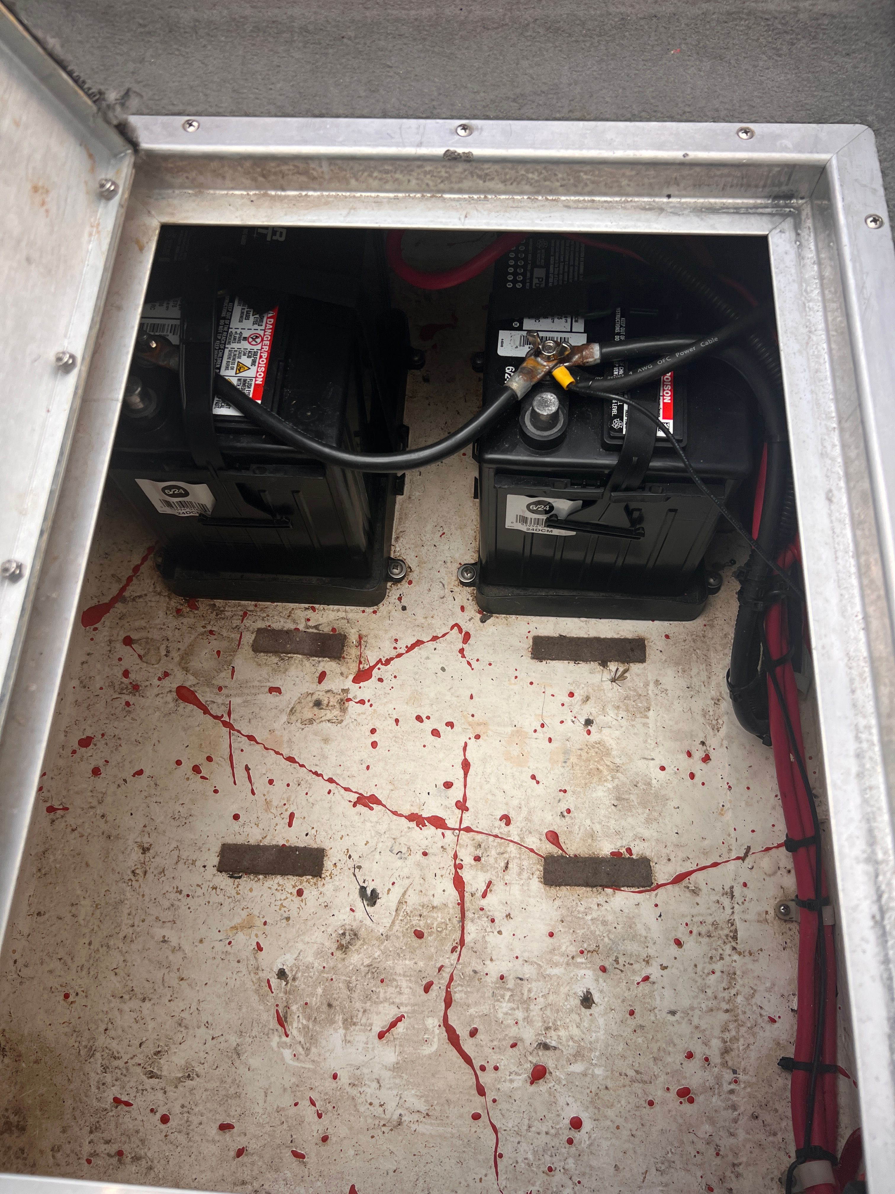 Boat battery compartment with two black batteries and red cables.