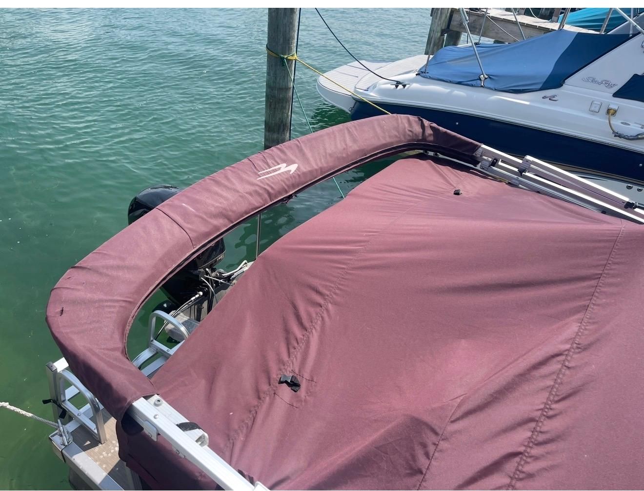 A 2018 Bennington 18SL with a maroon boat cover, docked at a pier in clear water.
