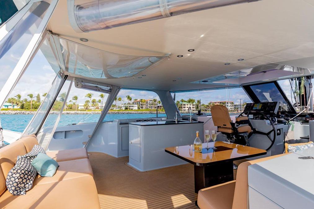 Luxurious 2018 Gunboat 57 yacht interior with seating, table, and helm, overlooking scenic waterfront.