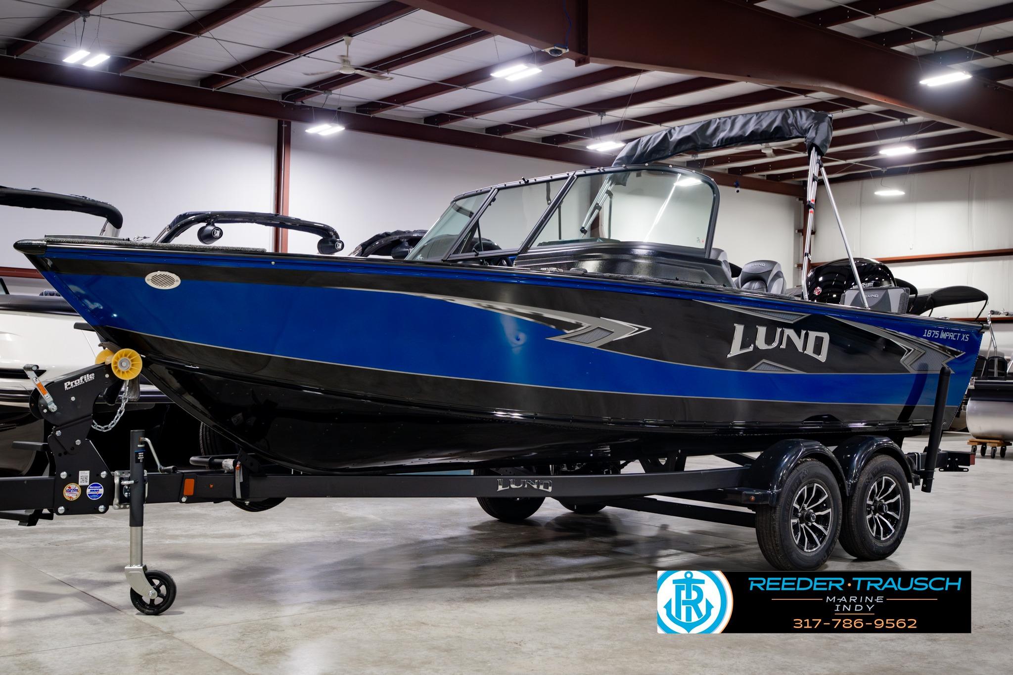 2026 Lund 1875 Impact XS boat in showroom, blue and black design, on trailer.