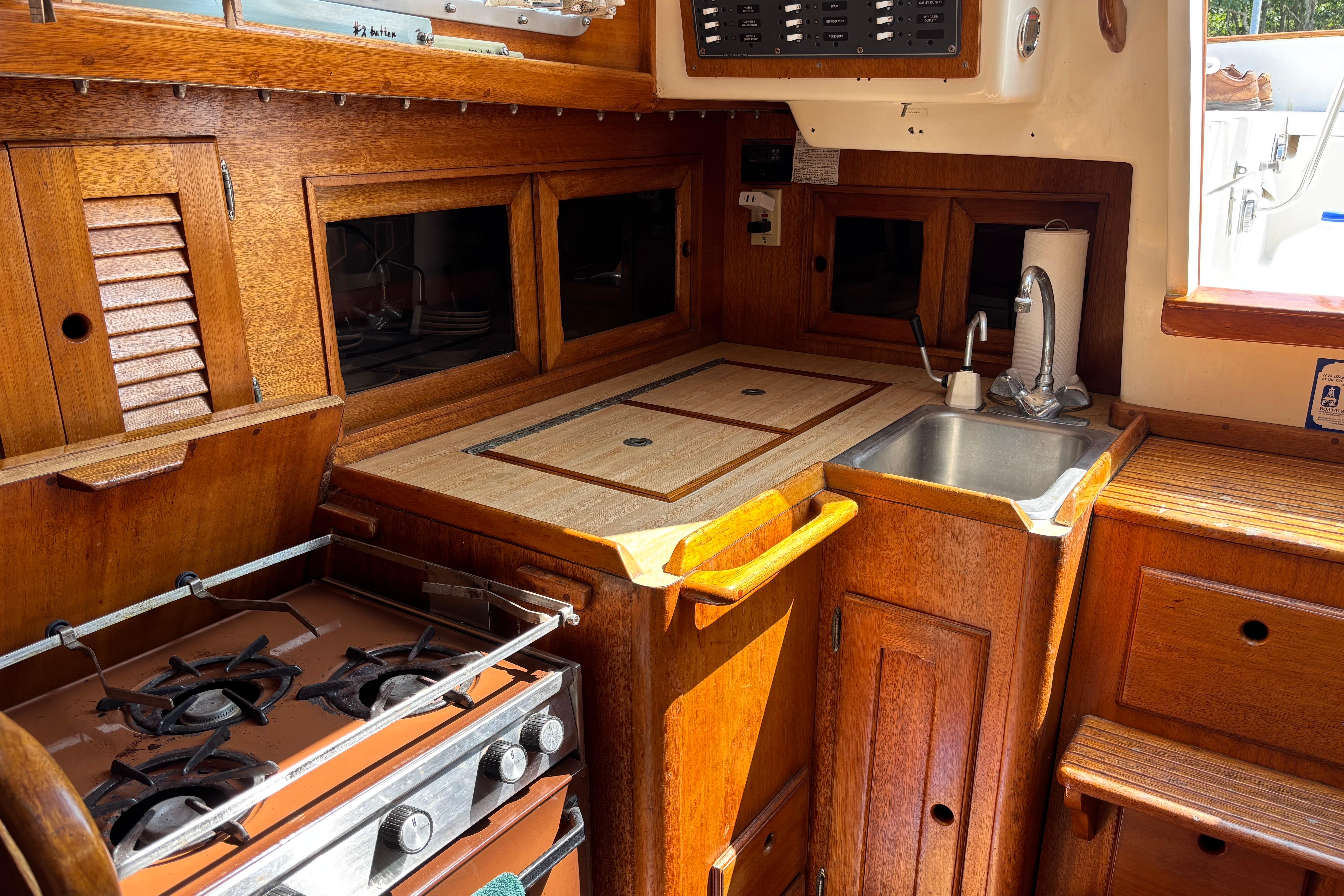 1979 Bristol 35.5 yacht kitchen with wooden cabinetry, stove, and sink.