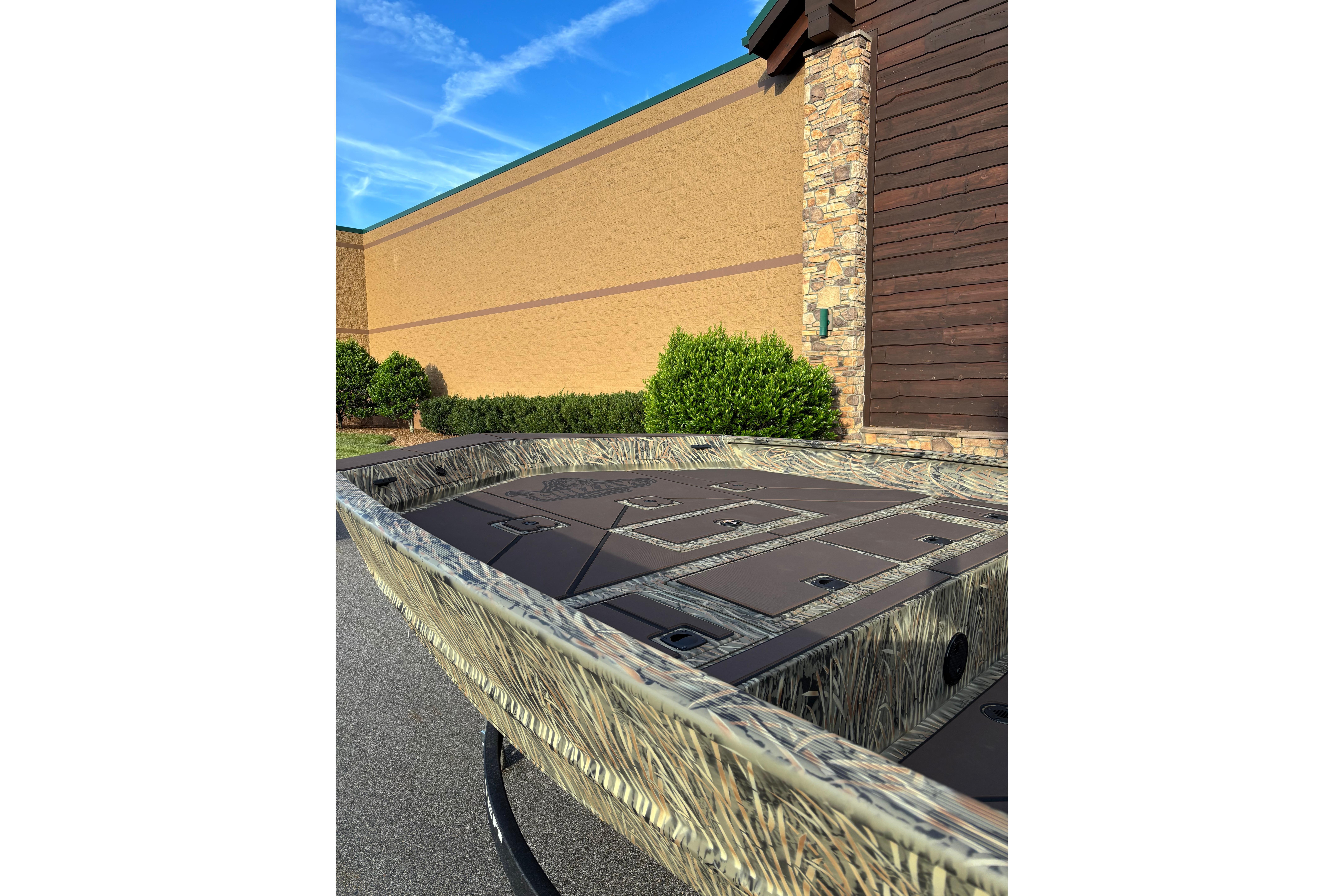 2026 Tracker Grizzly 2072 CC boat with camouflage design, parked outdoors near a building.