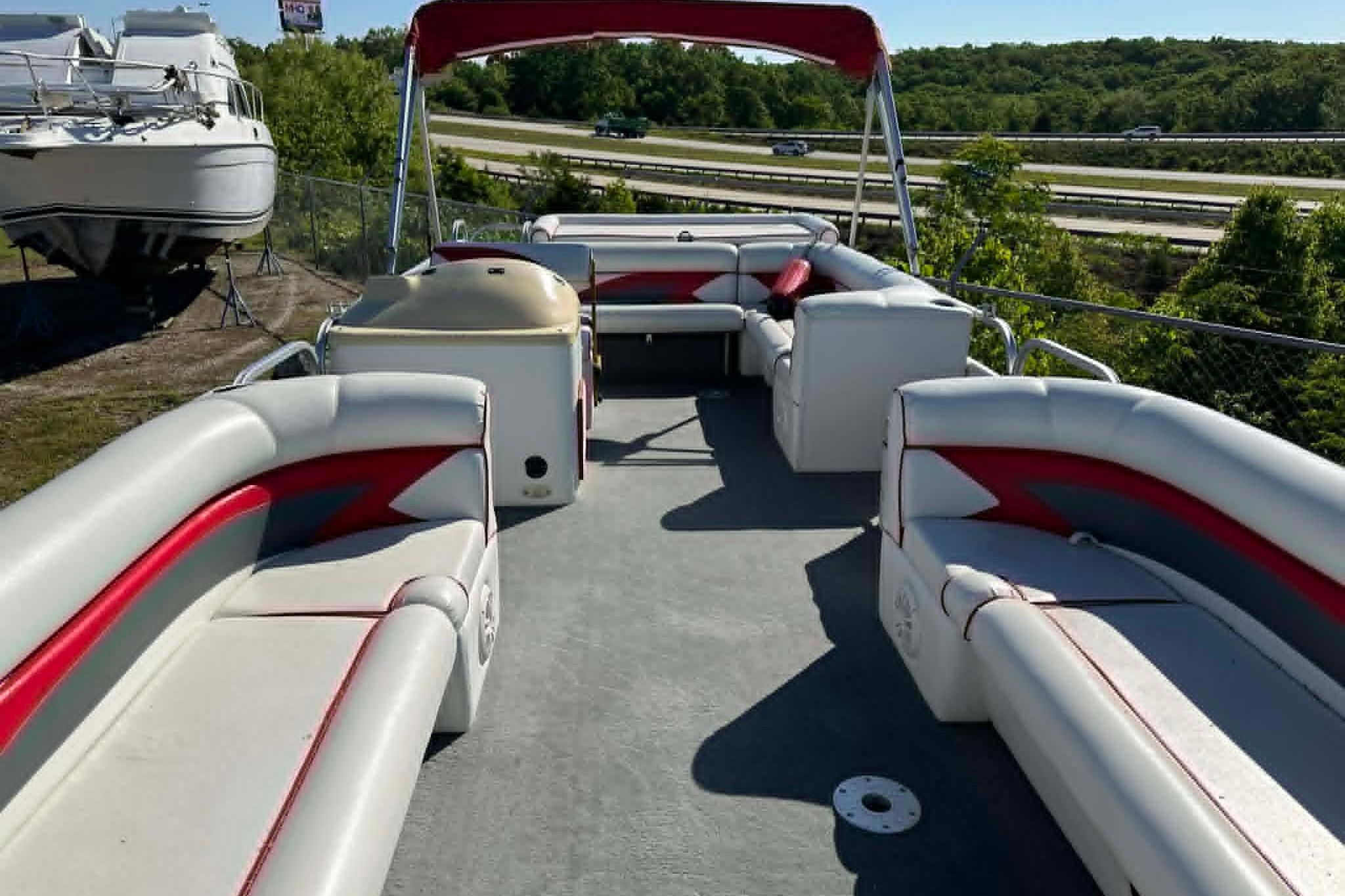 1999 PlayCraft Sport 2400 pontoon boat with red and white seating, docked outdoors.