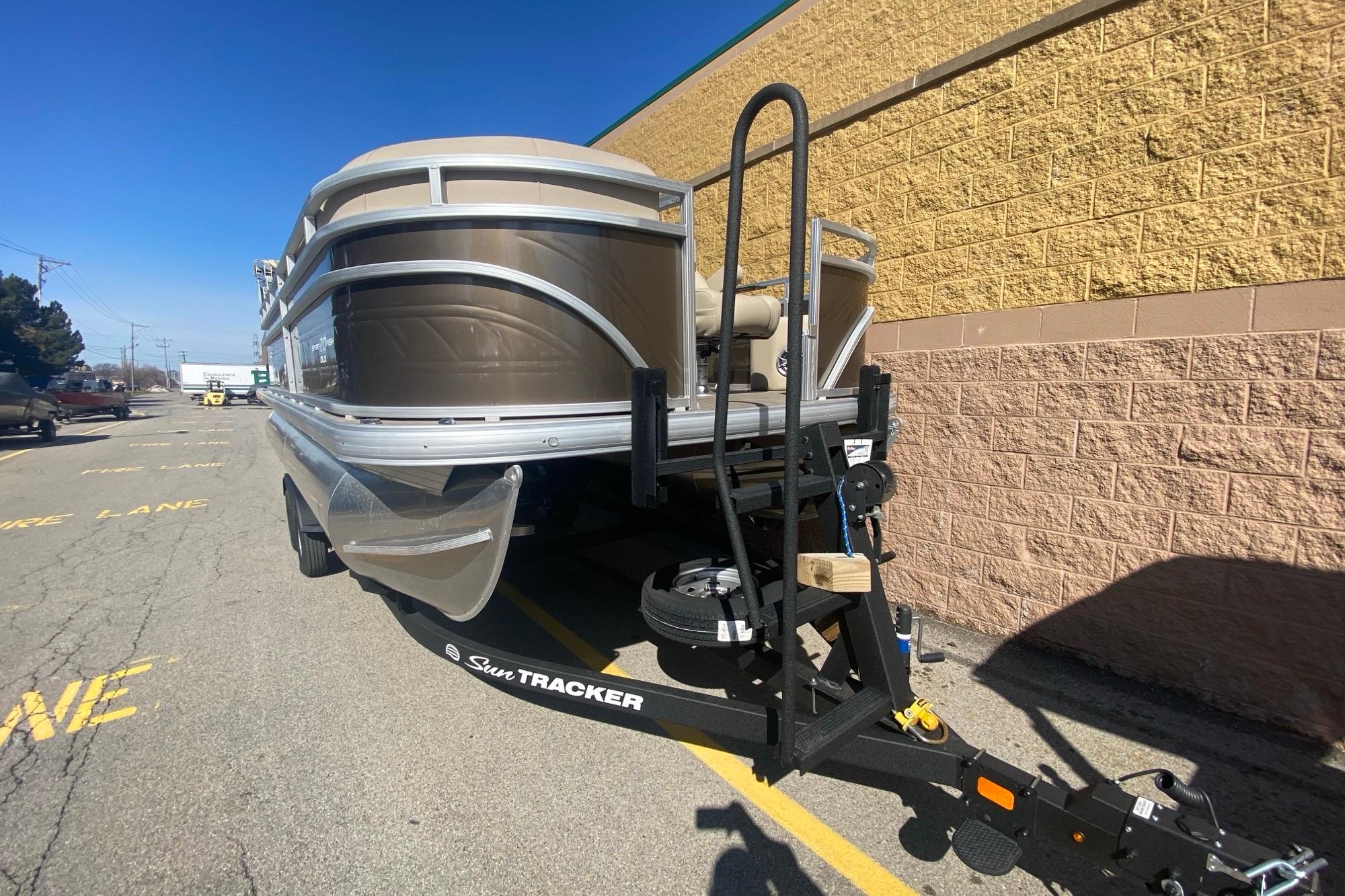 2025 Sun Tracker SportFish 20 DLX pontoon boat on trailer, parked outdoors.