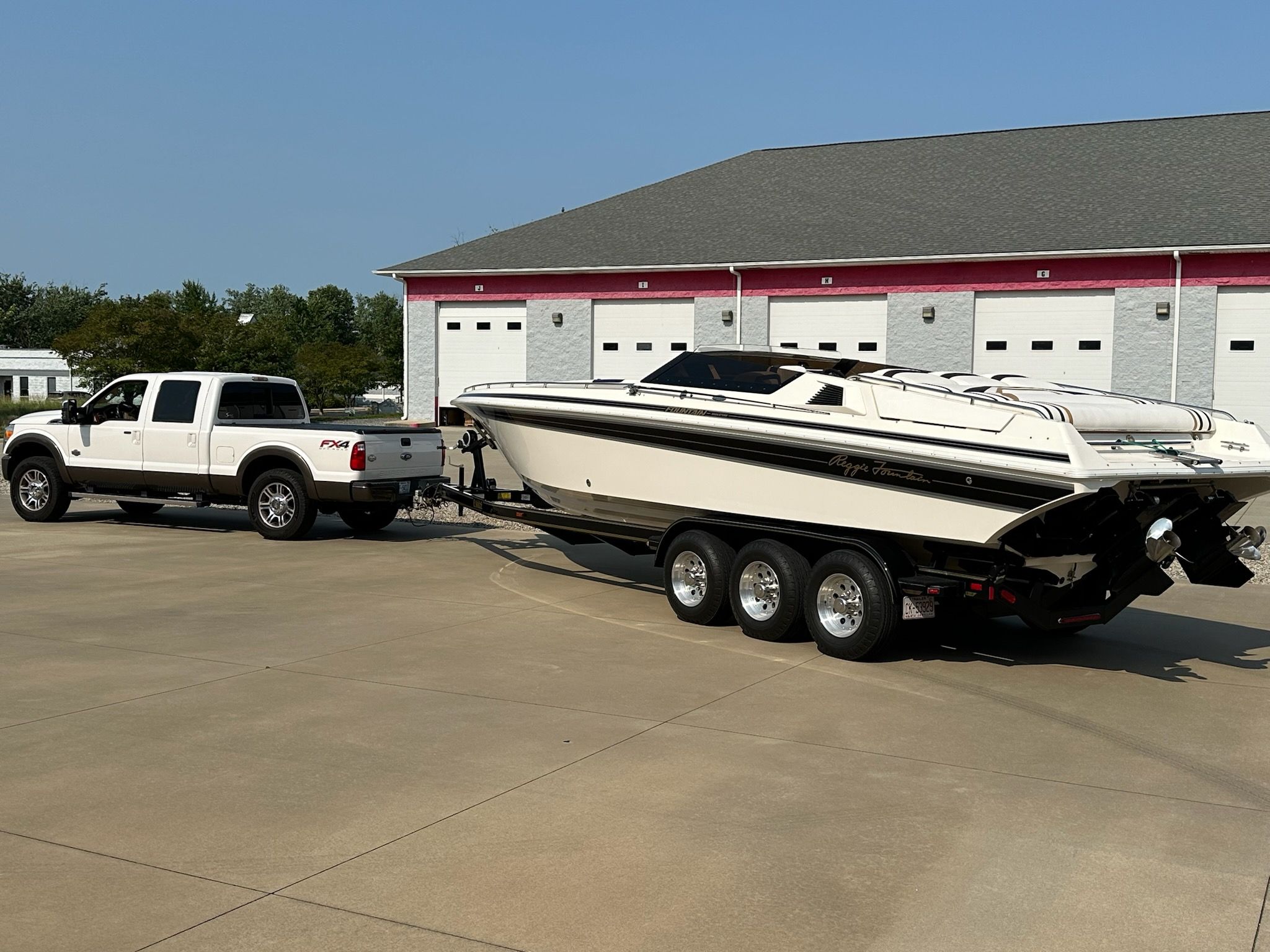 White truck towing 1992 Fountain Fever boat on trailer in parking lot.