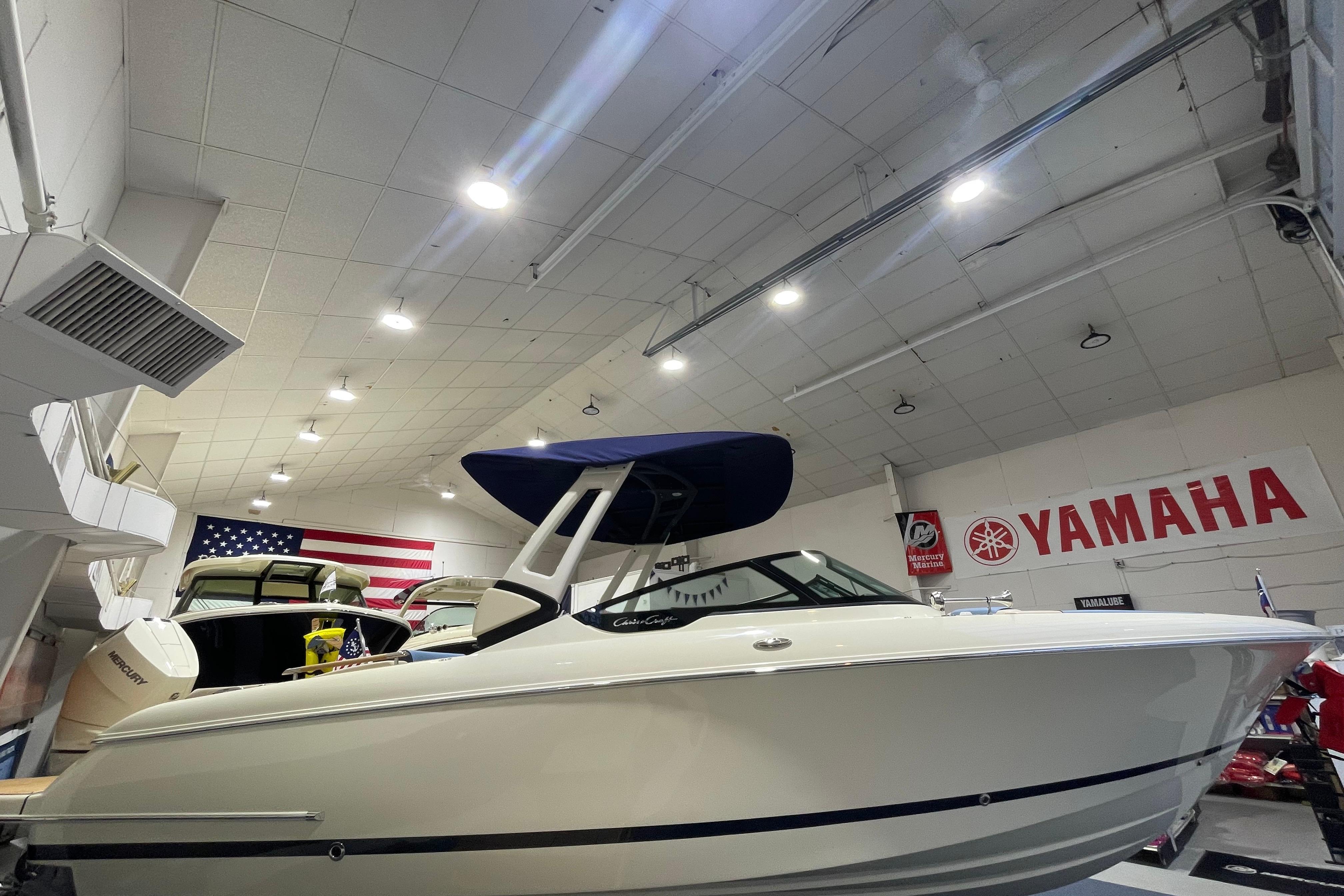 2026 Chris-Craft Sportster 28 boat displayed indoors with Yamaha signage and American flag.