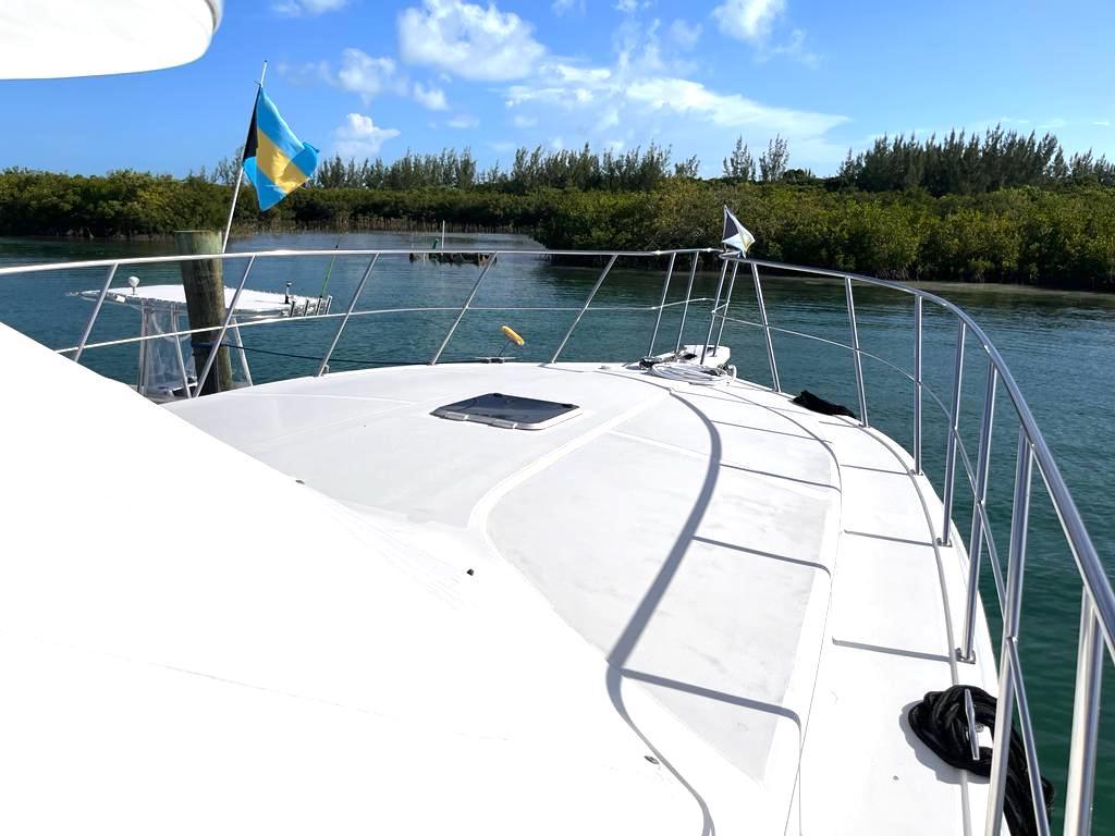 1998 Navigator 53 yacht deck with flags, cruising through scenic waterway under blue sky.