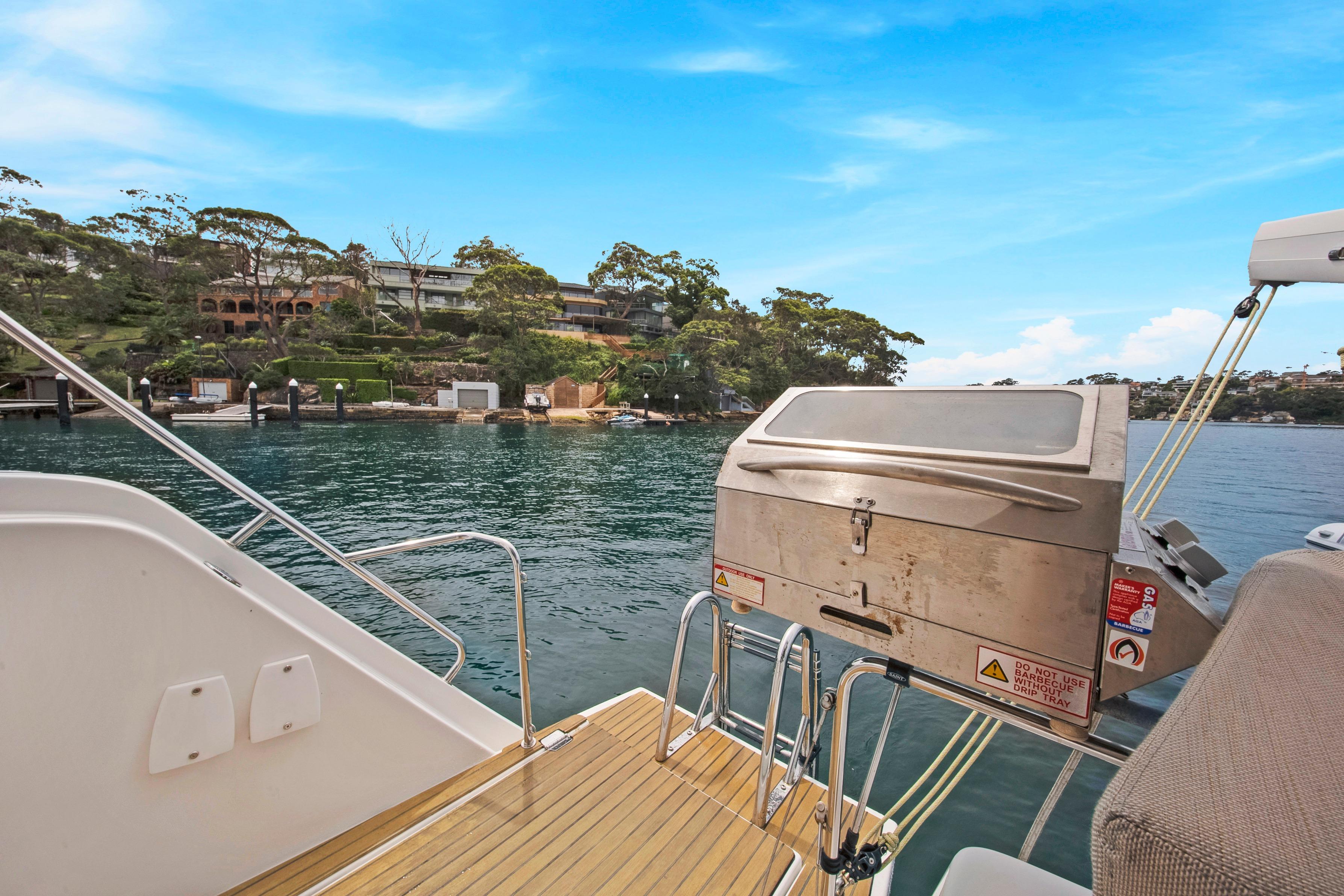 Aventura 37 yacht deck with barbecue grill, overlooking serene waterfront and lush greenery, 2023 model.