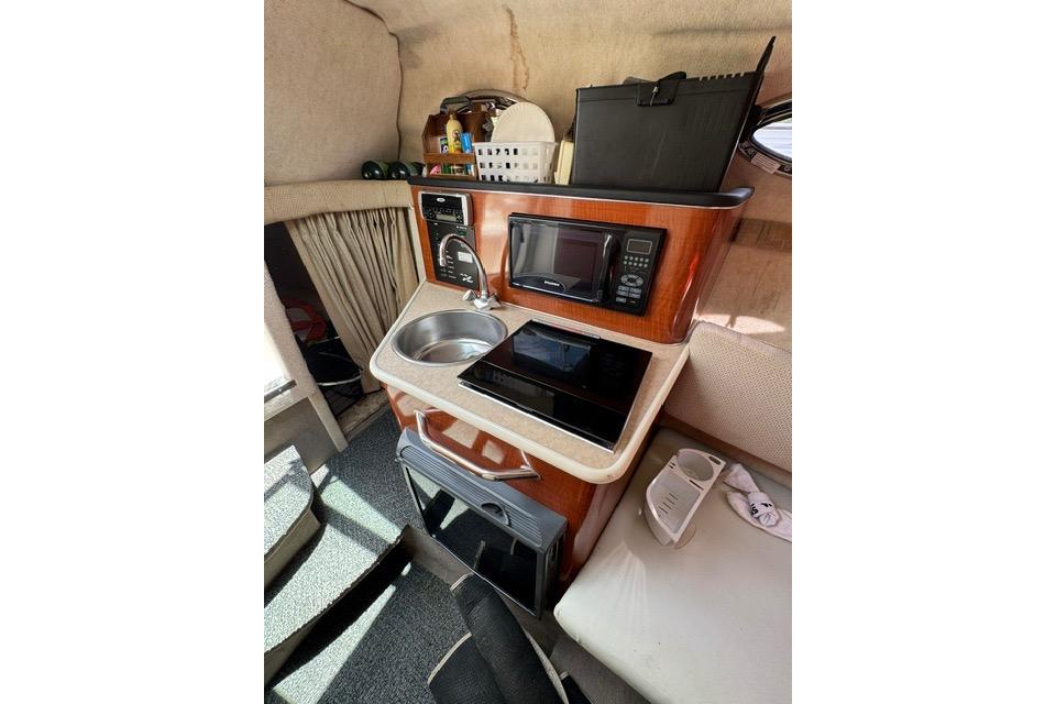 Compact kitchen area in a 2004 Sea Ray 240 Sundancer boat, featuring a sink and microwave.