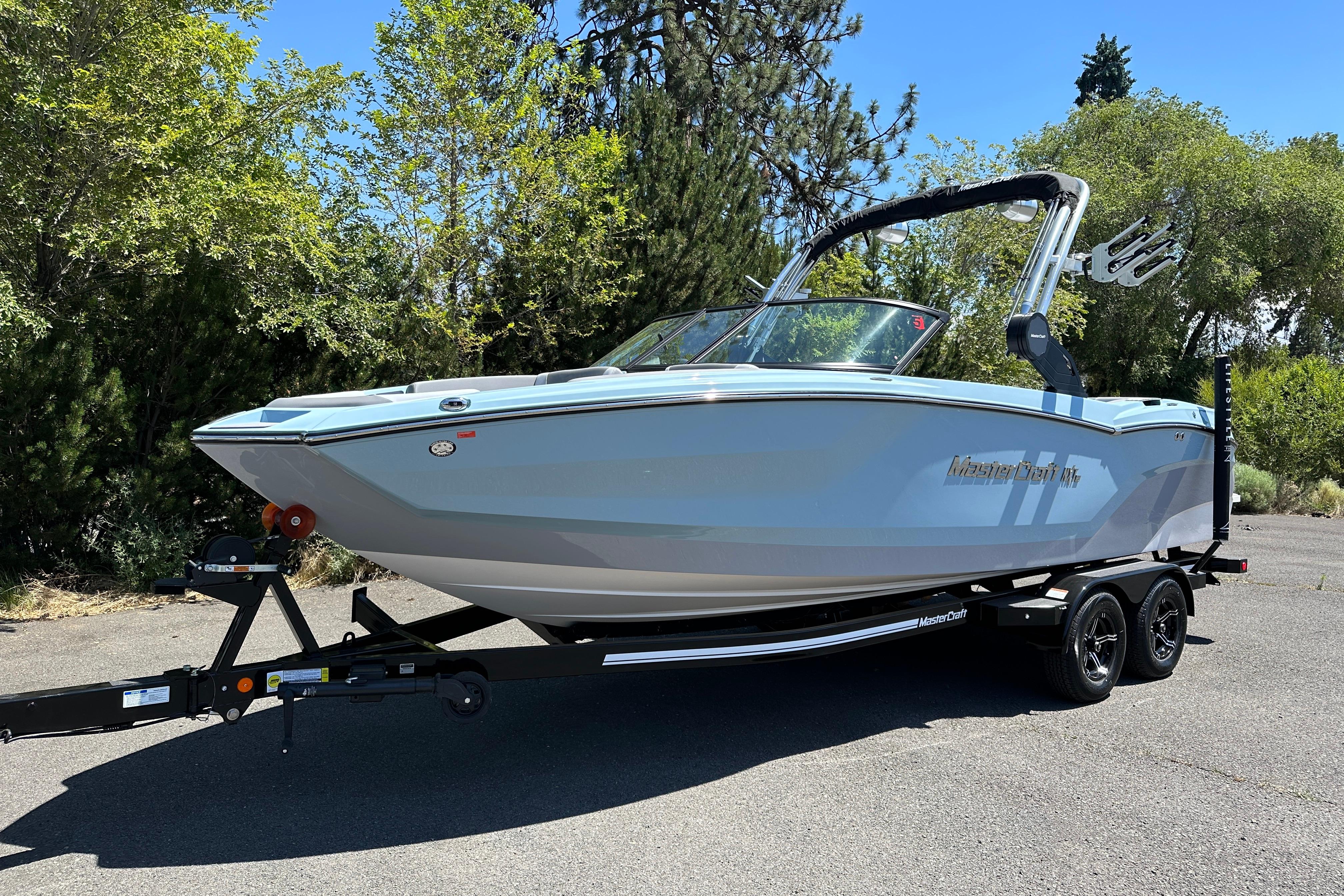 2023 MasterCraft NXT23 boat on trailer, parked outdoors with trees in the background.