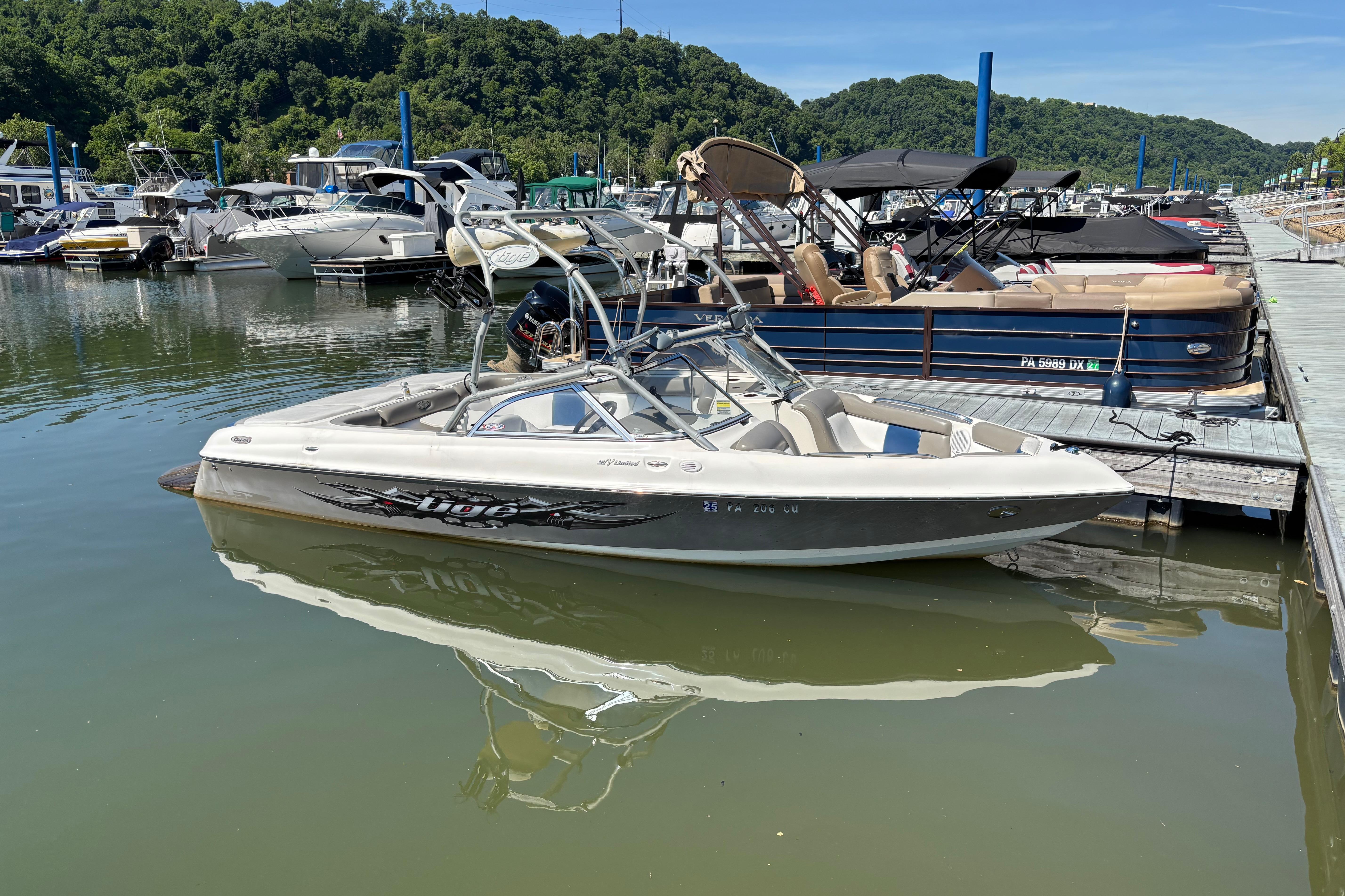 2004 Tigé 22V Limited Edition boat docked at a marina with lush green hills.