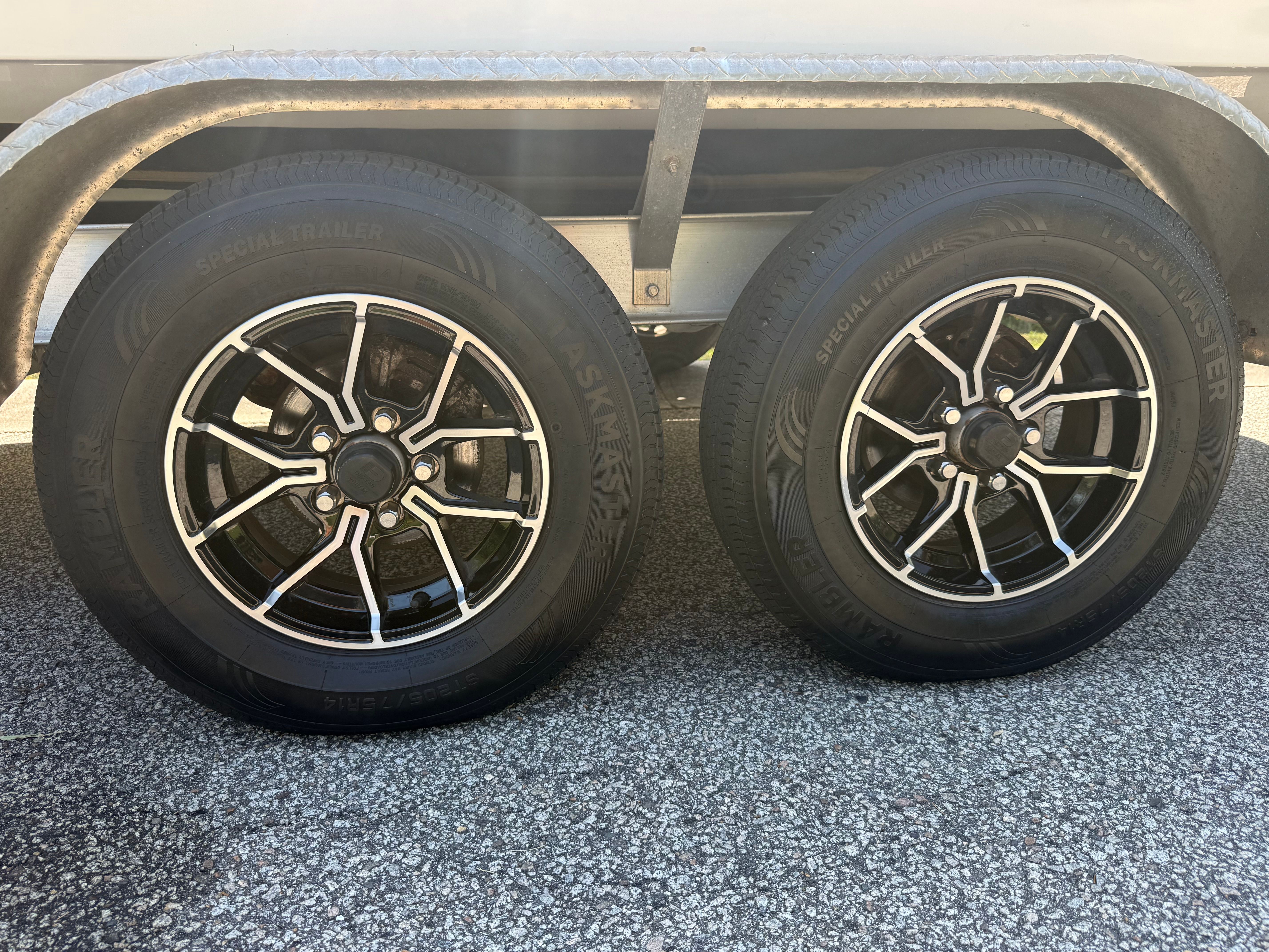 Two black tires with silver rims on a trailer, set on a paved surface.