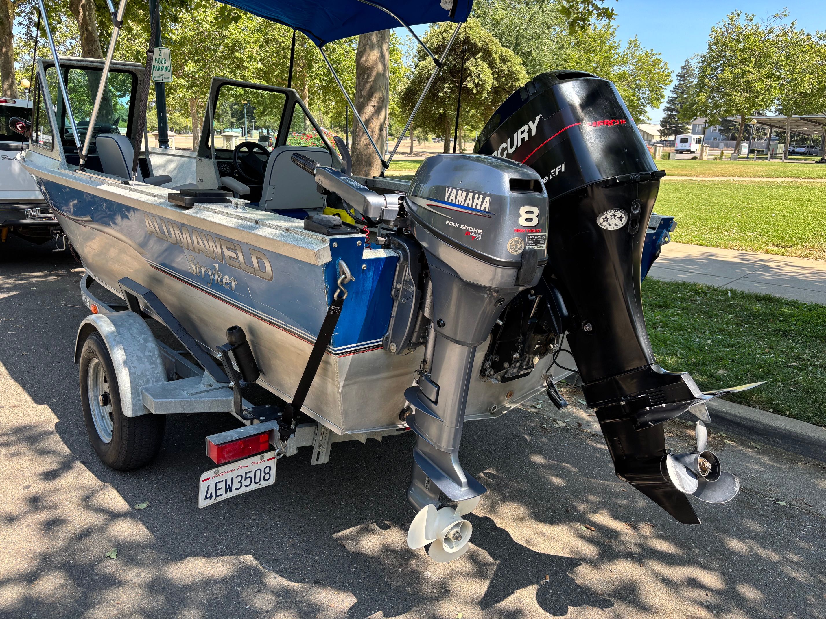 A 2002 Stryker Rogue boat with two outboard motors, parked on a trailer in a park.