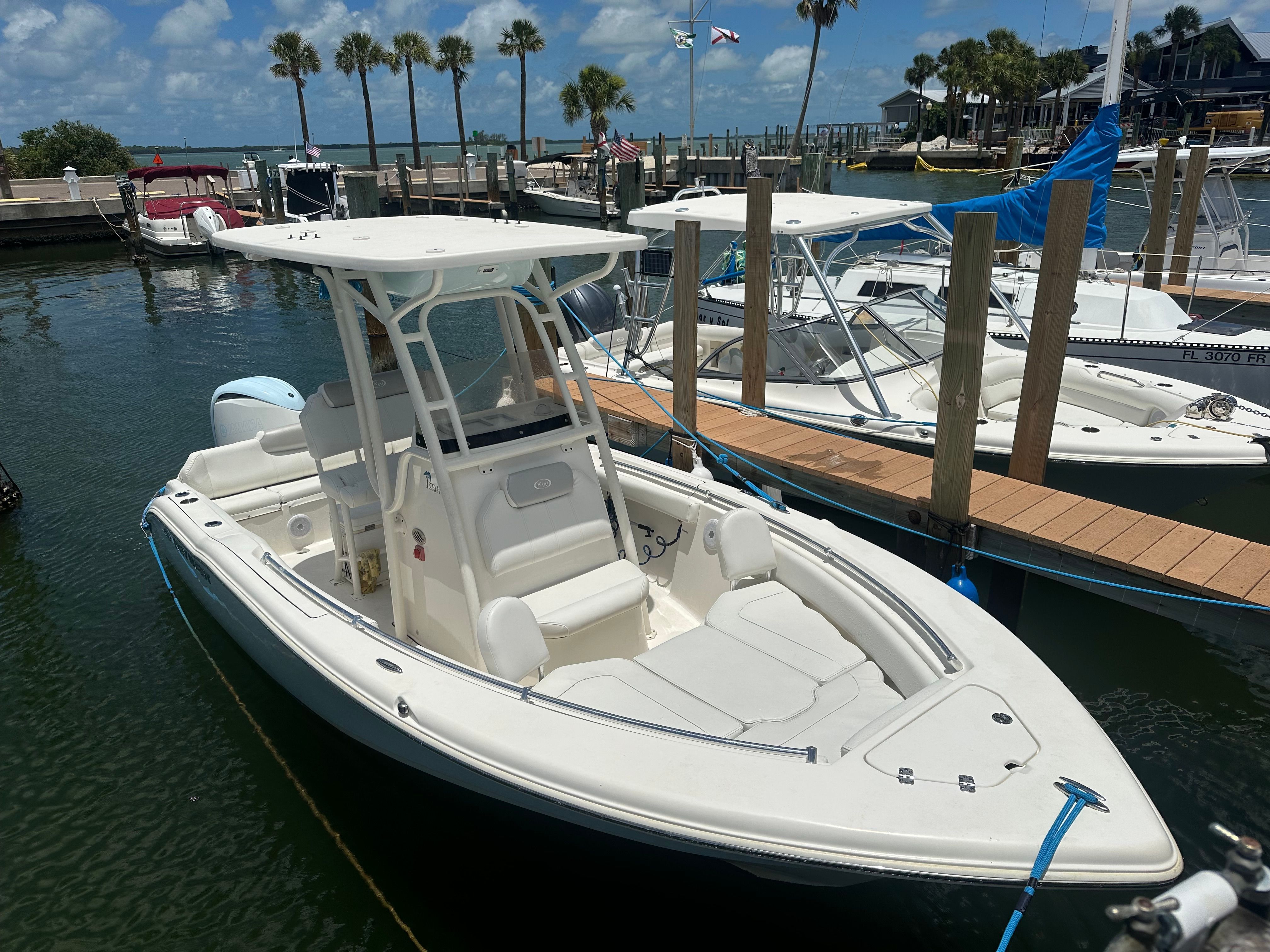 A white motorboat is docked in a calm marina with palm trees in the background.