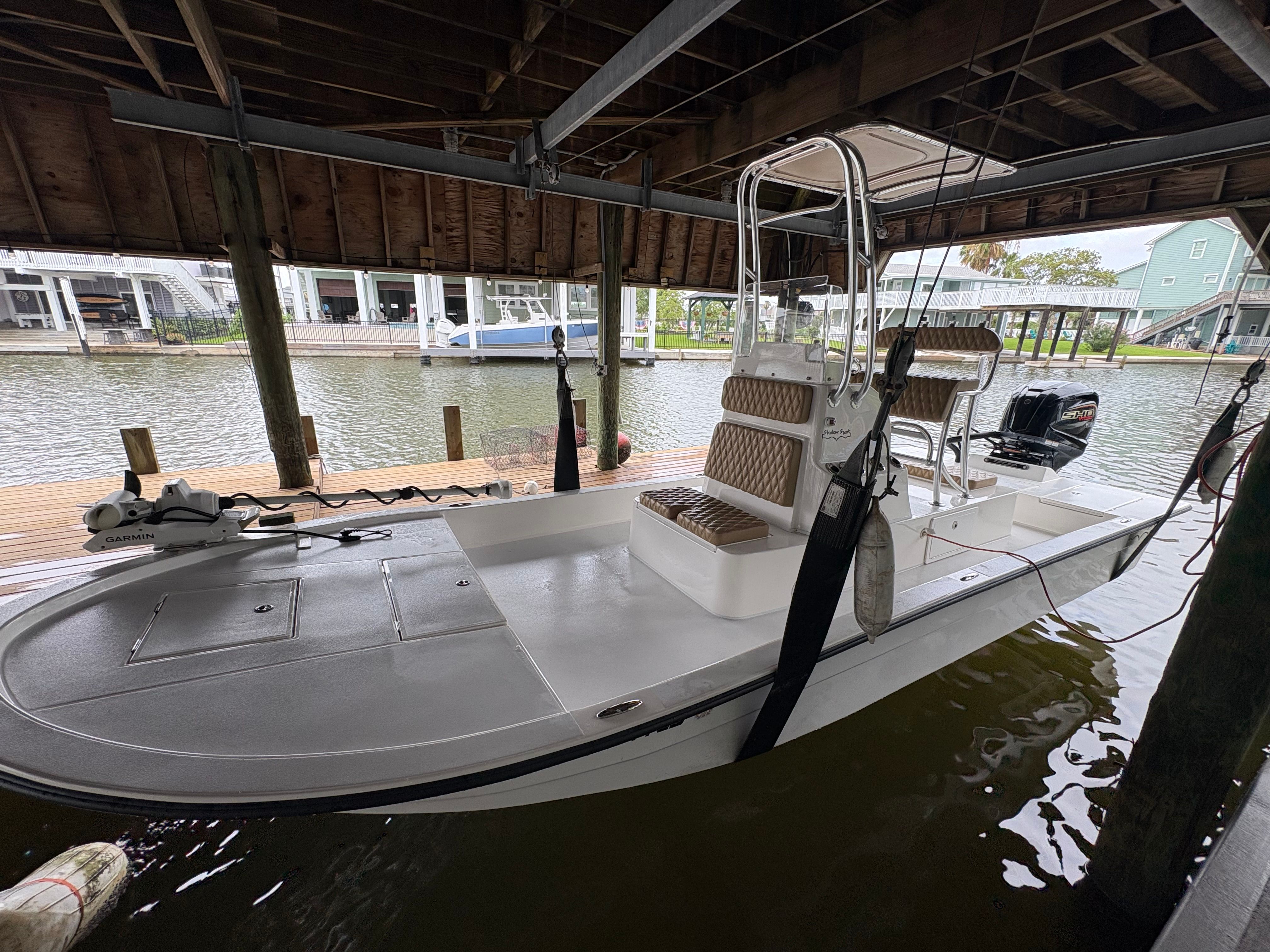 A 2025 Shallow Sport 24 Sport boat is docked under a covered area by the water.