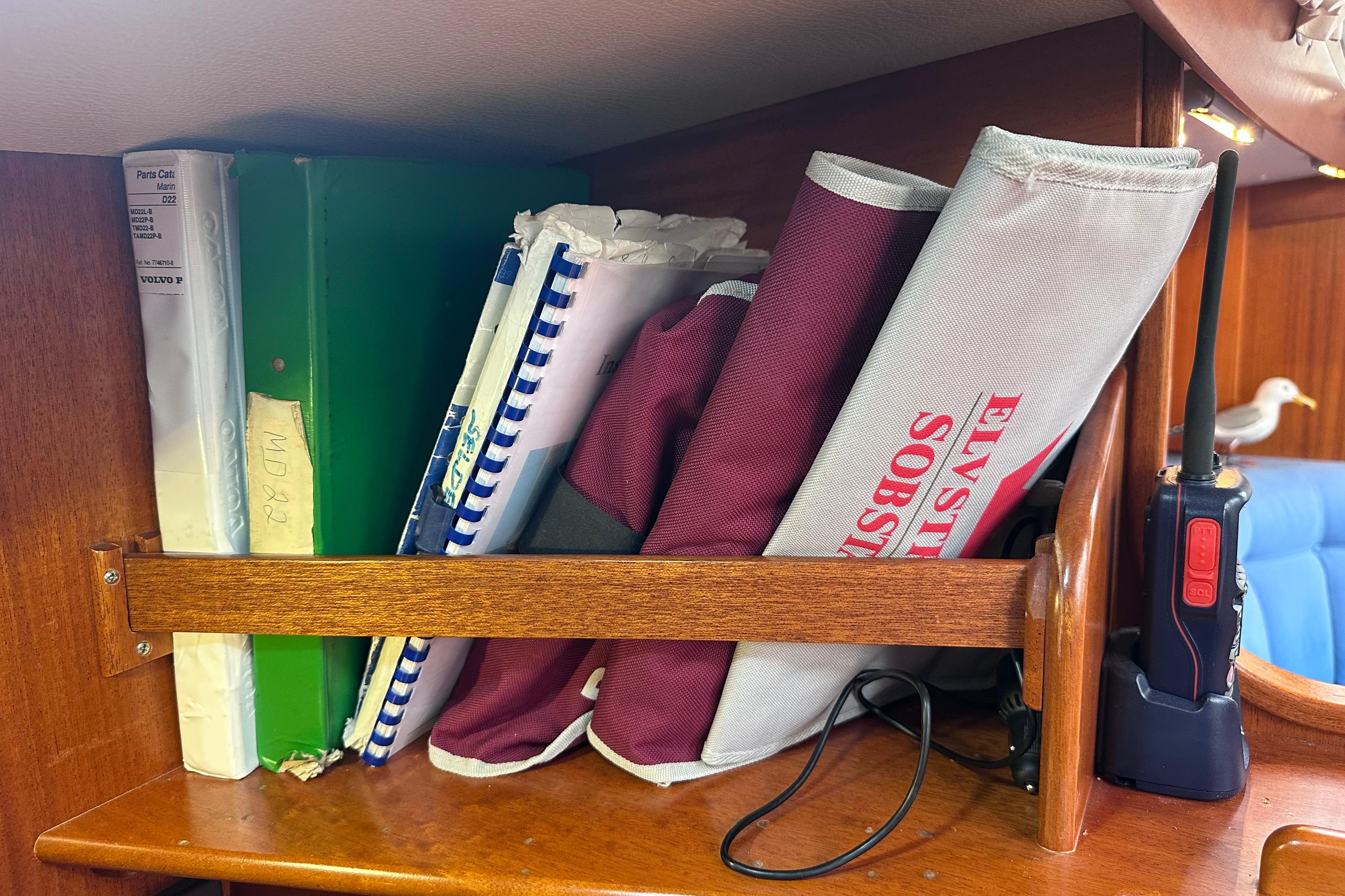 Shelf on 1999 Hallberg-Rassy 39 yacht with manuals, binders, and a radio.