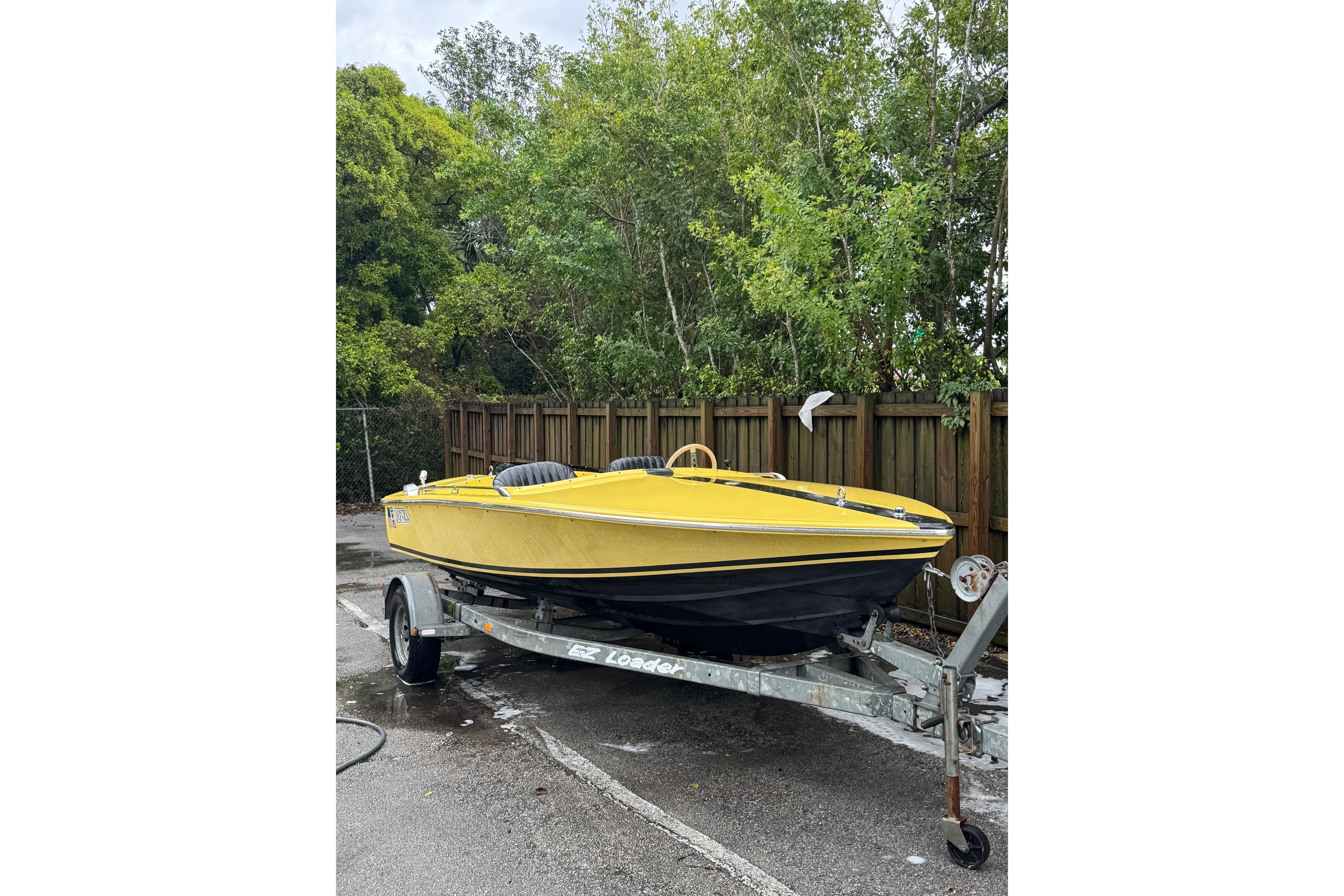 Yellow 1987 Donzi 16 Classic boat on trailer, parked near wooden fence and trees.